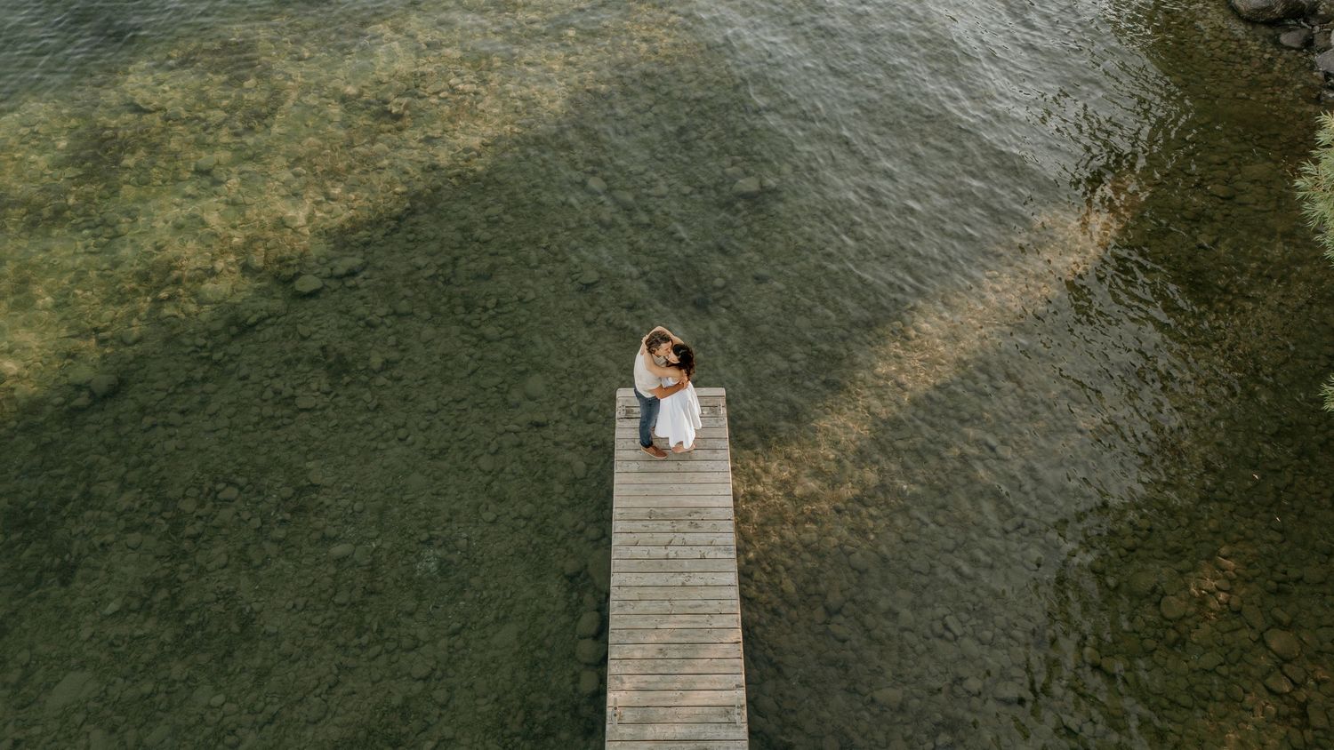 Wooden boardwalk stretches over a serene lake surrounded by lush greenery and trees in a peaceful natural setting.