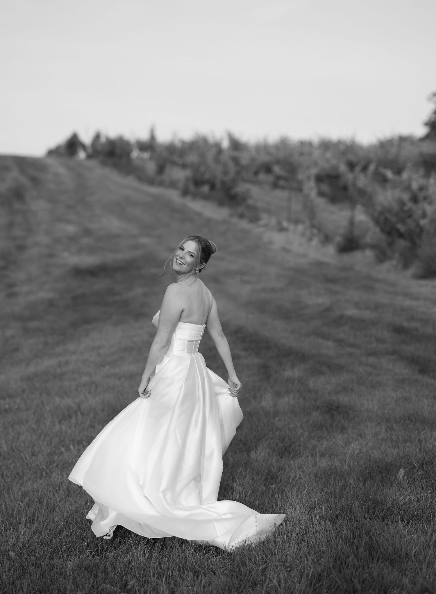 Bride twirling in white dress on grassy hillside in black and white.