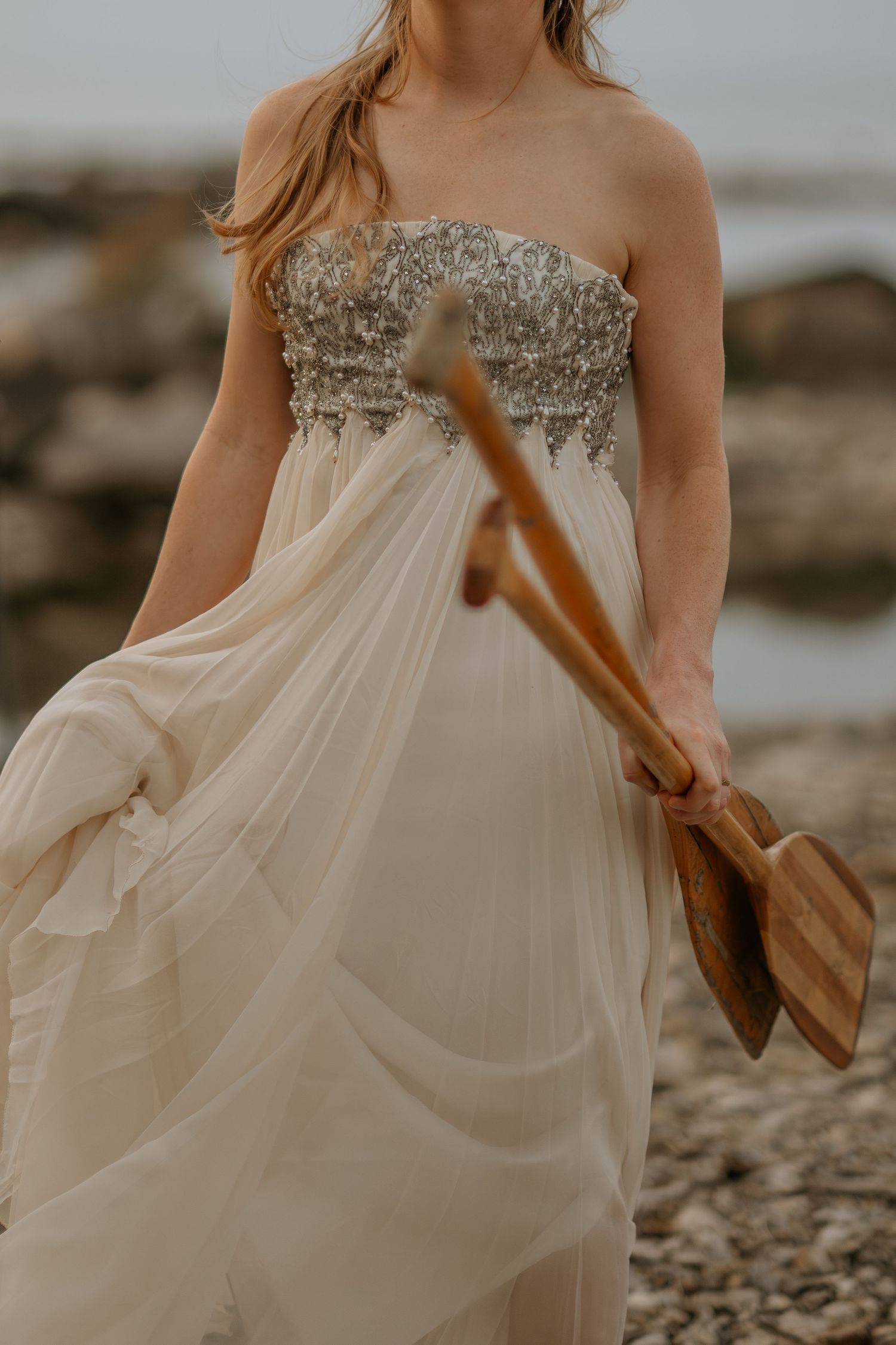 Flowing white wedding dress with embellished bodice detail shown in a series of close-up shots on a beach.