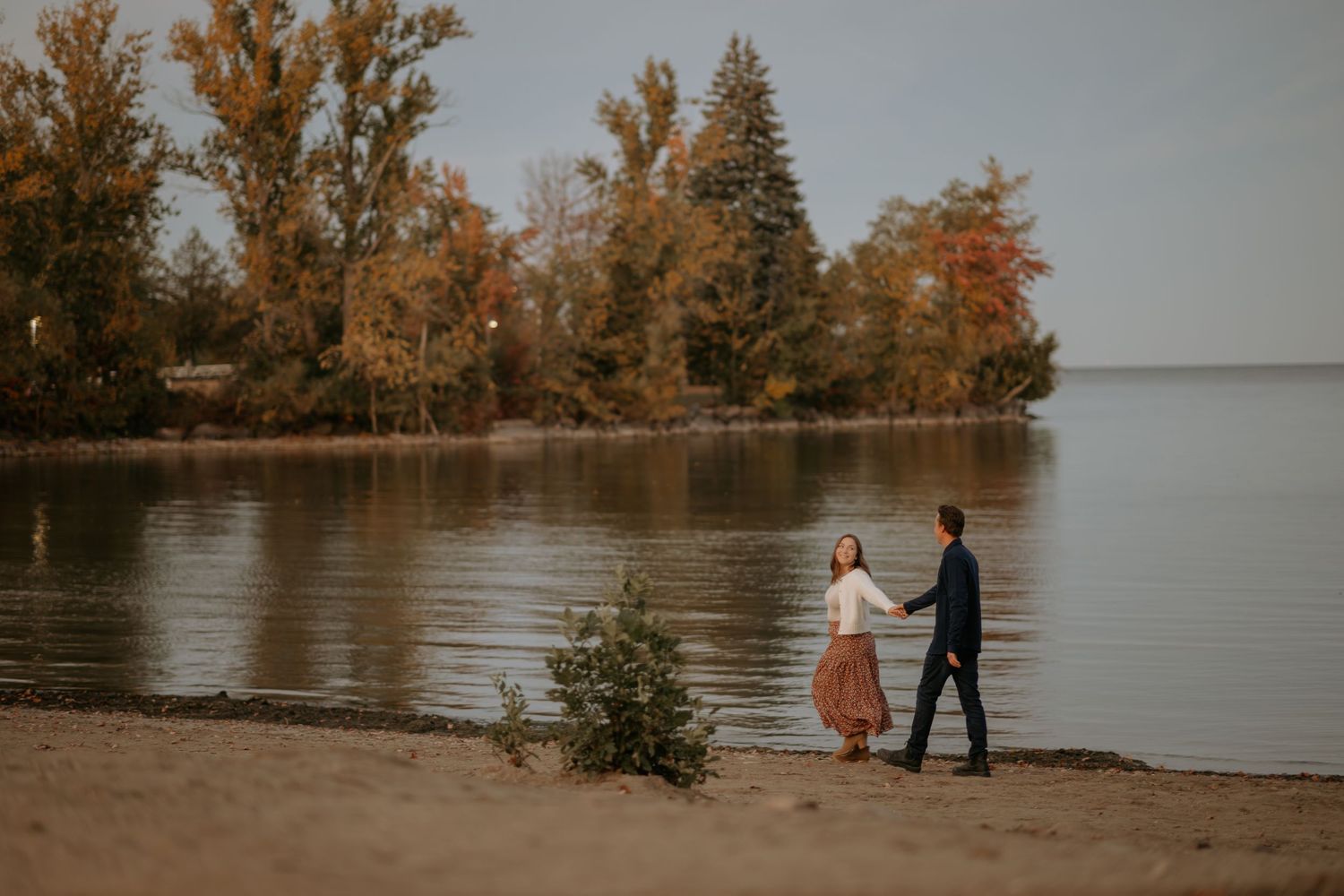 Autumn trees line a serene lakeside during golden hour.