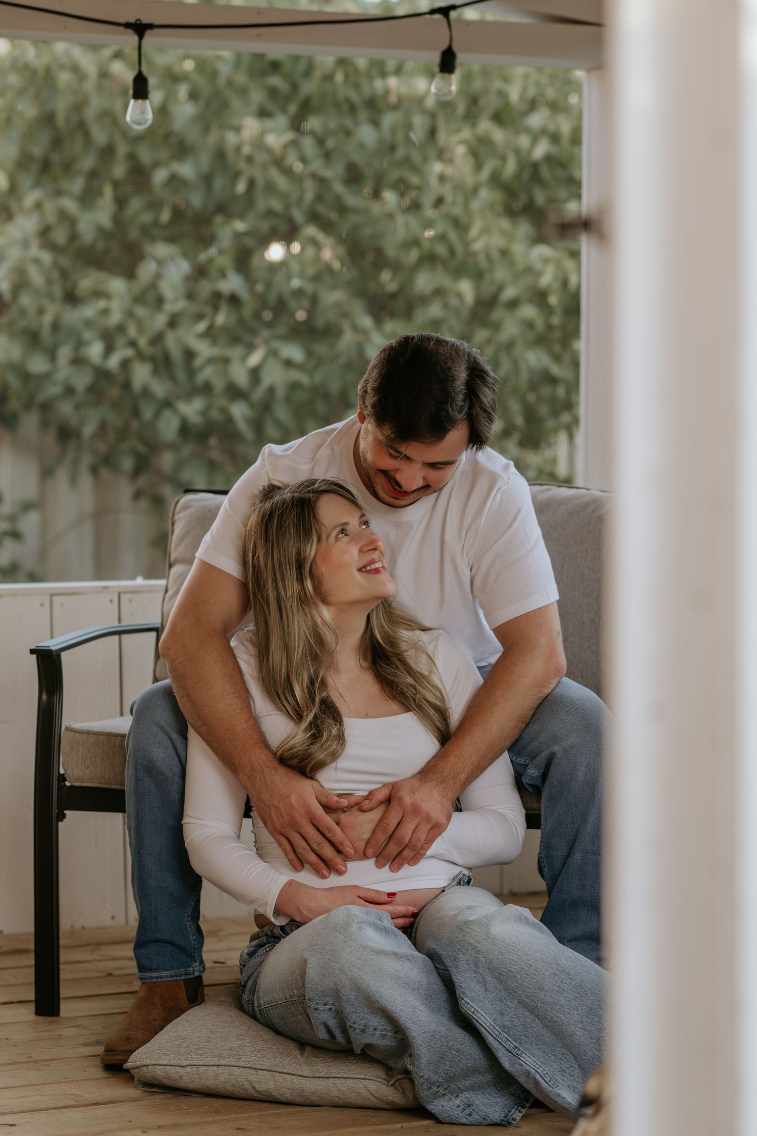 Couple relaxing on cushions during indoor maternity session with white columns in background.