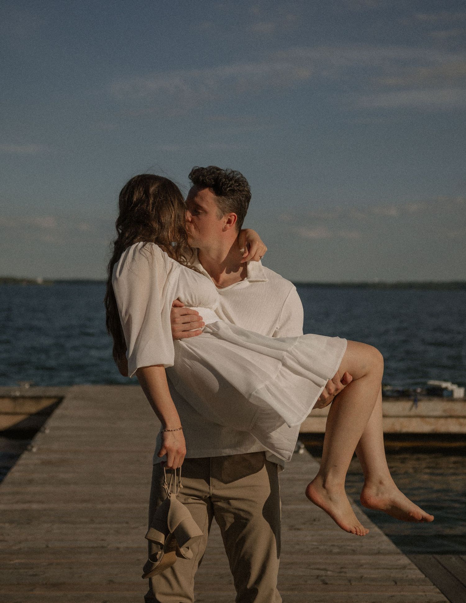 A romantic embrace shared between a couple on a wooden dock at sunset.