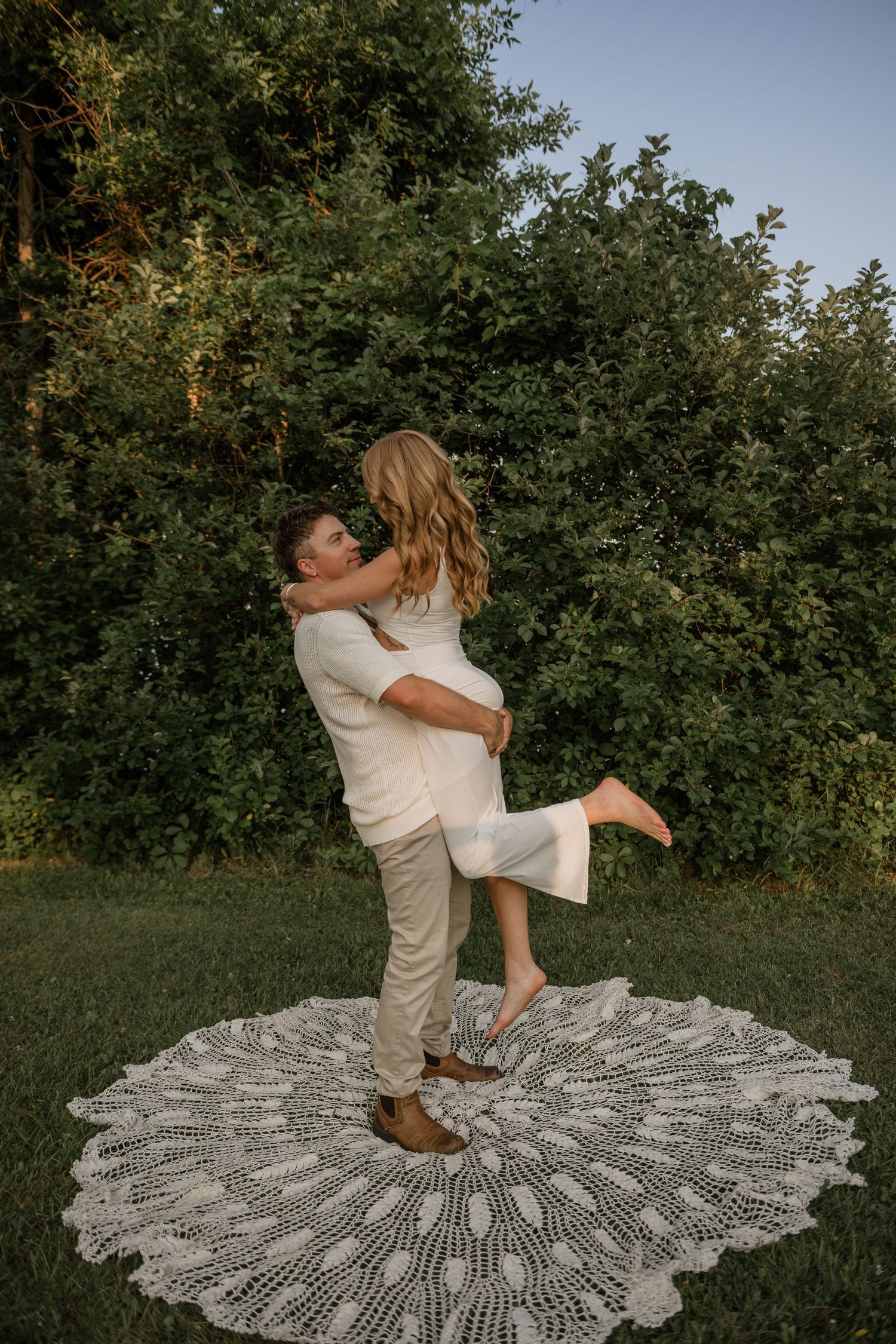 Couple dances and twirls on decorative lace blanket in garden setting.