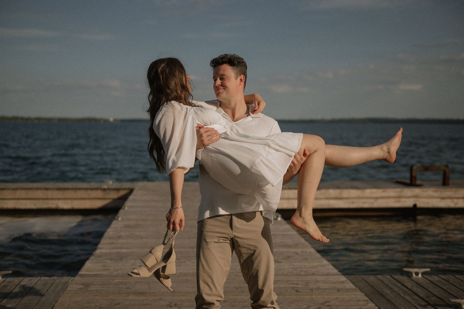 A playful moment captured as a couple shares a romantic embrace on a lakeside dock.