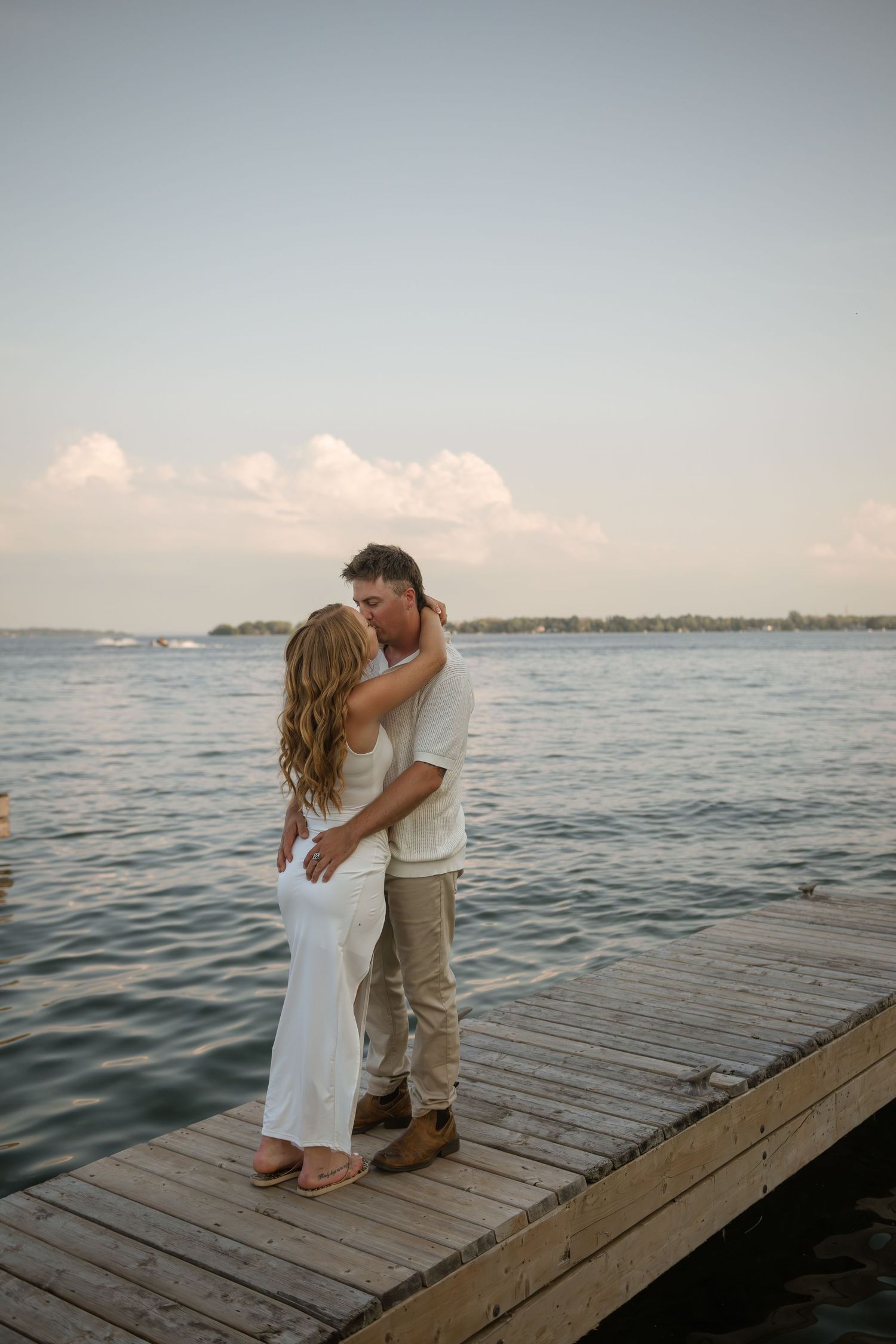 Couple shares romantic moments on wooden pier overlooking calm waters at dusk.