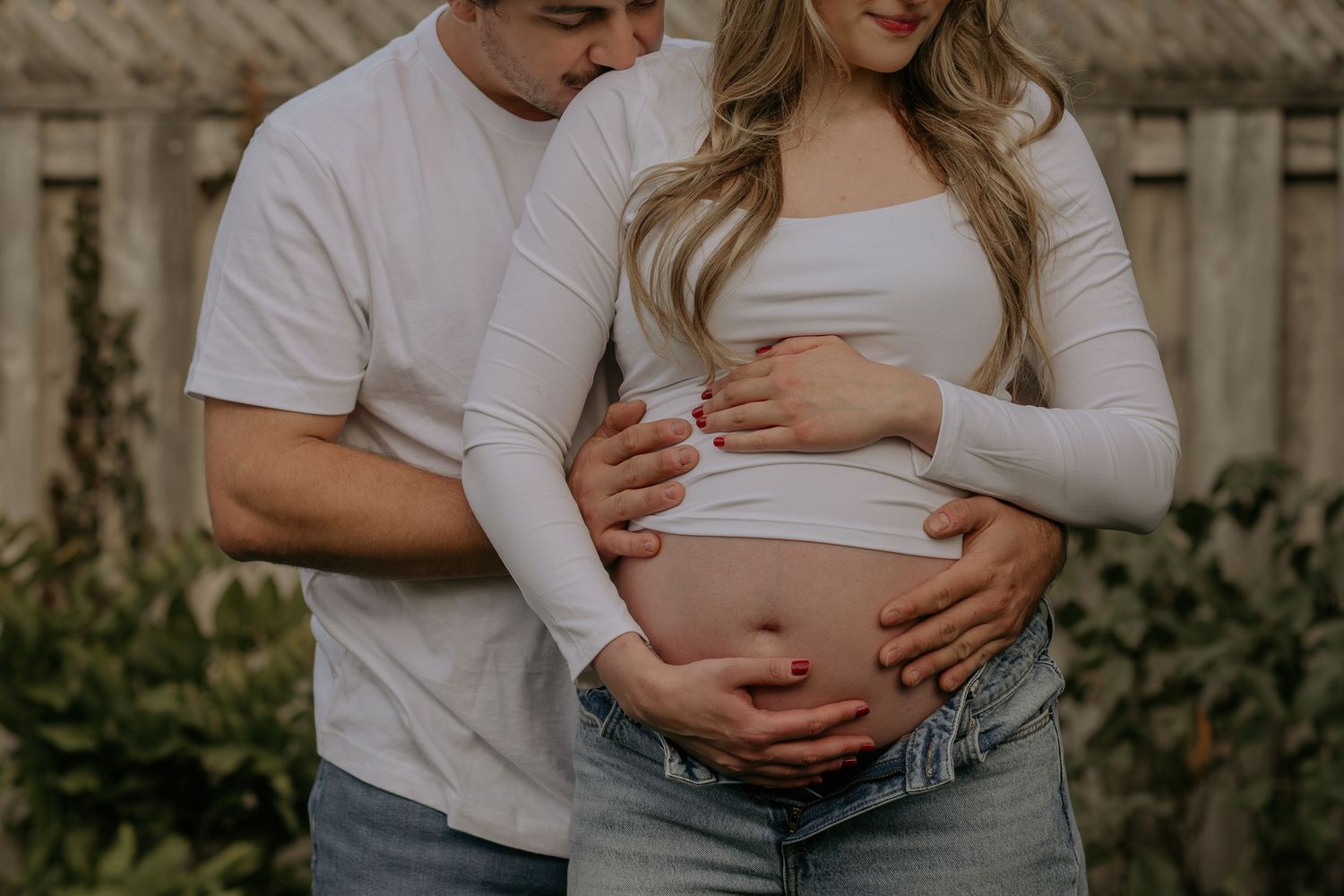 Intimate maternity photoshoot featuring couple in white and grey casual attire sitting on wooden deck.