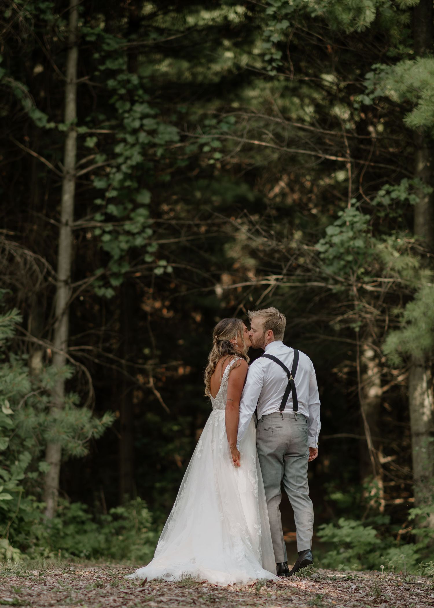 A couple in wedding attire shares an intimate moment on a wooded hillside in a natural forest setting.