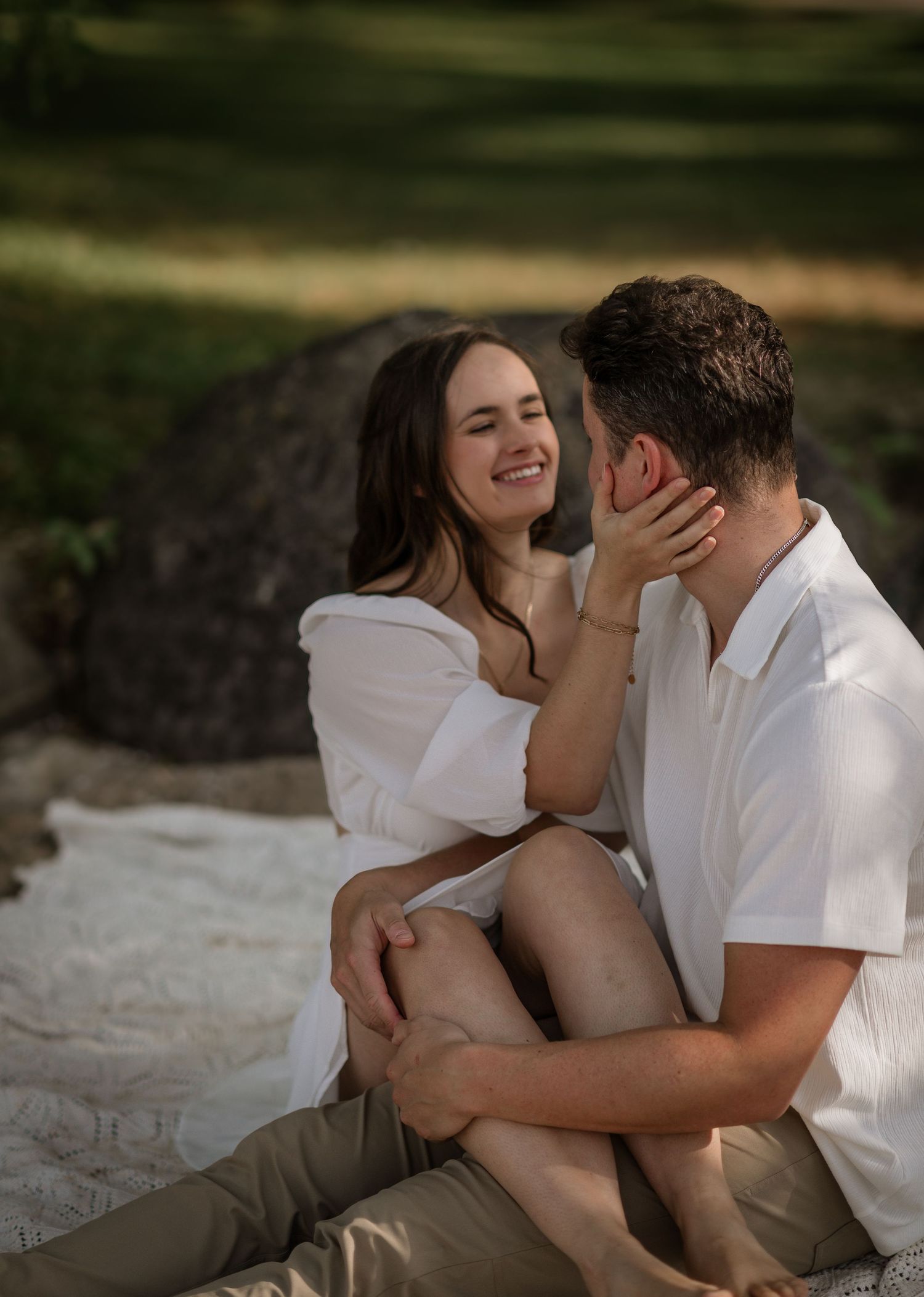 A romantic couple shares an intimate moment while sitting together outdoors on a sunny day.