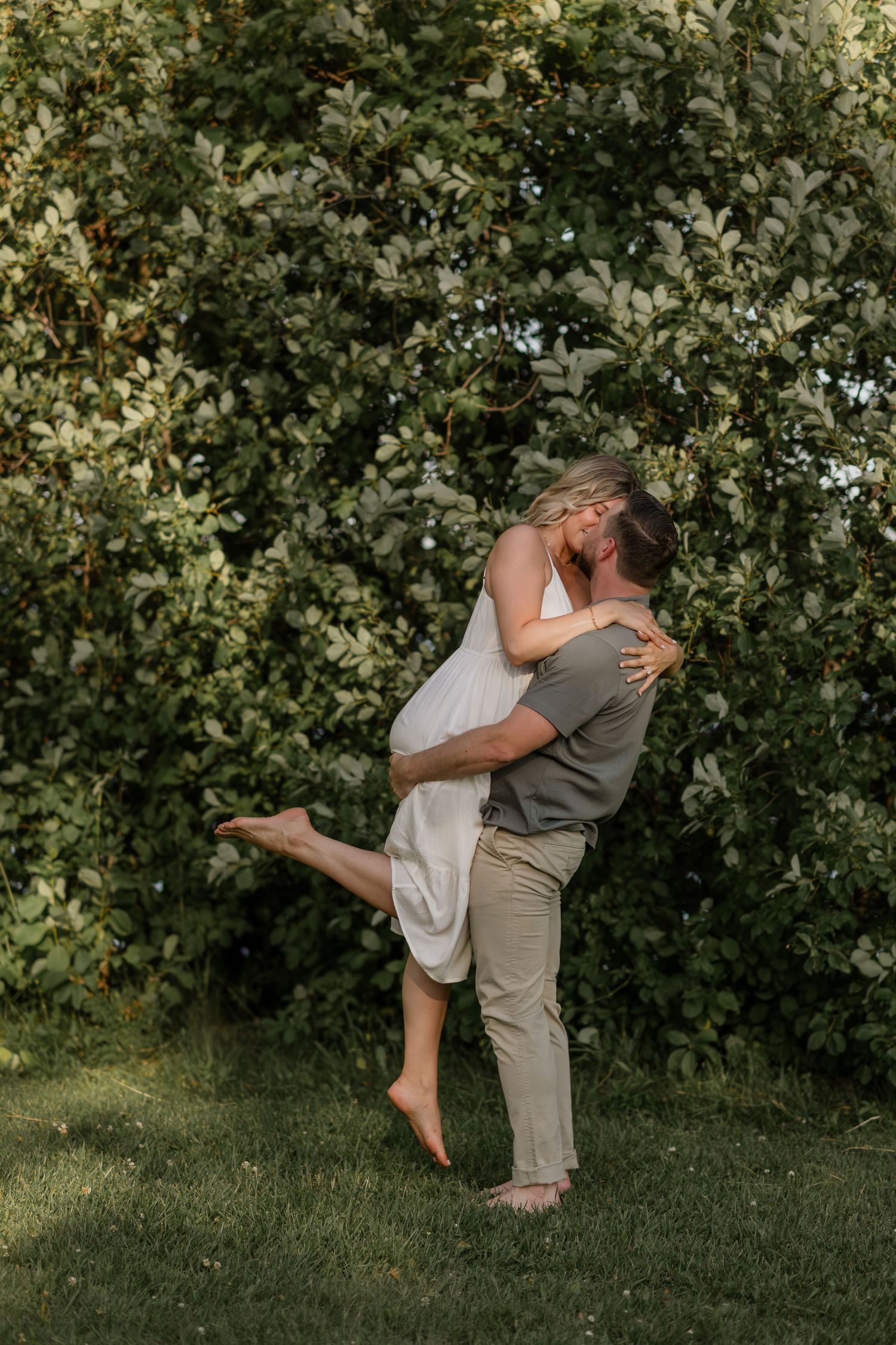 Playful couple dances together on grassy lawn with lush green foliage background.