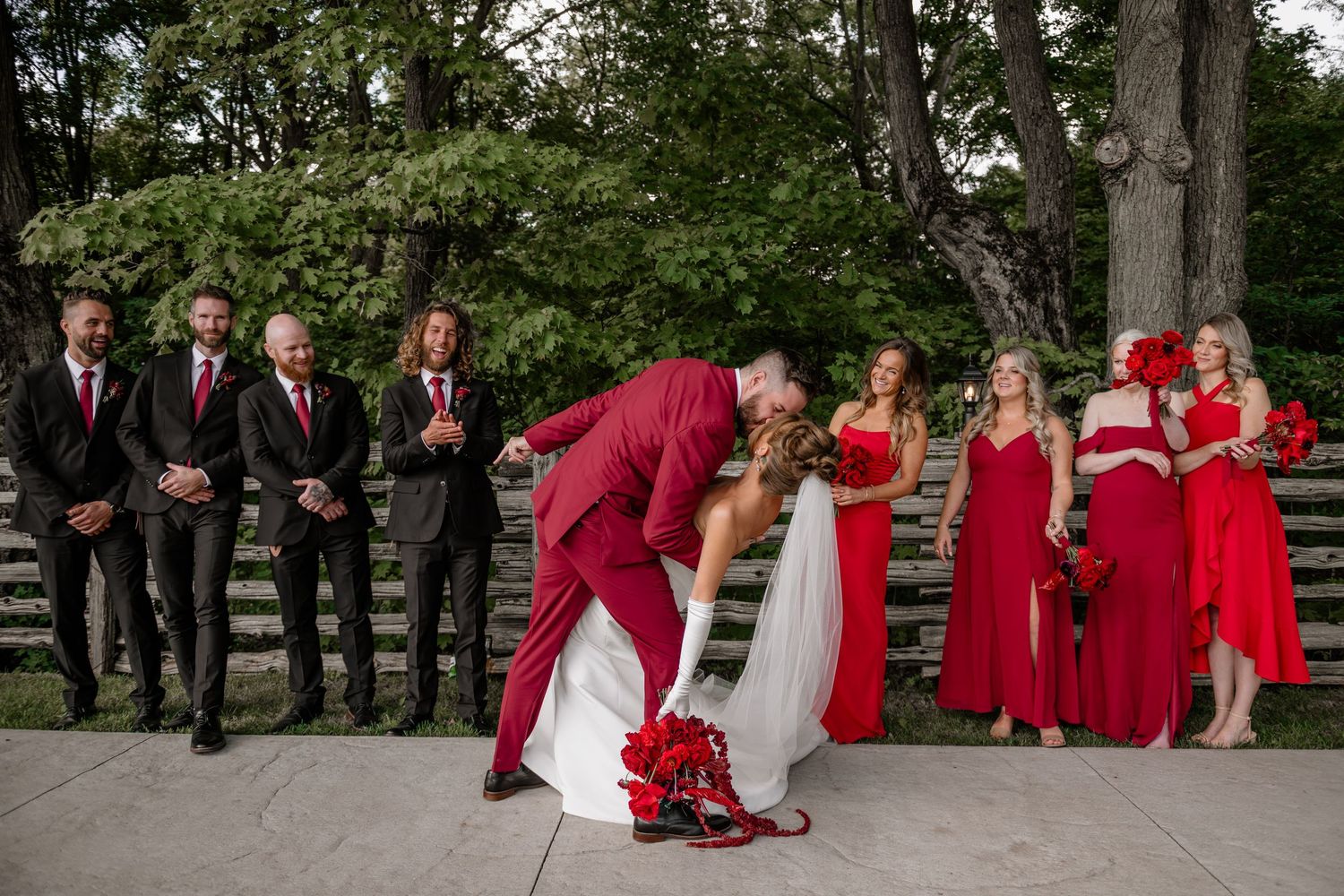 Wedding party in burgundy and white formal attire posed outdoors on garden grounds.
