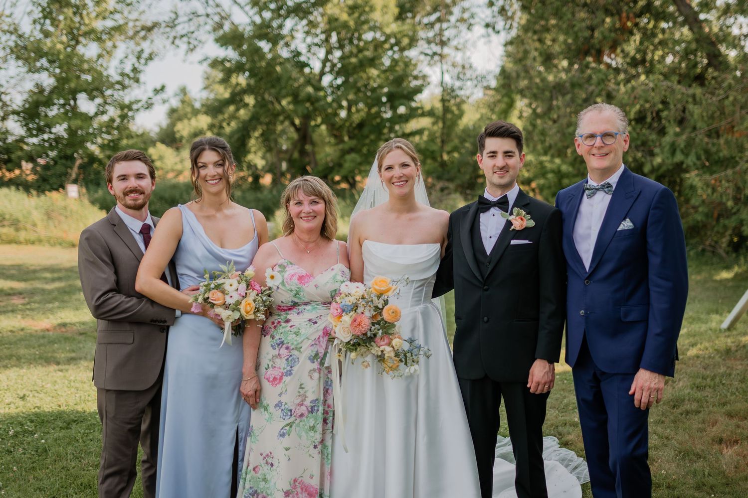 Wedding party poses together on grassy lawn during summer outdoor celebration.