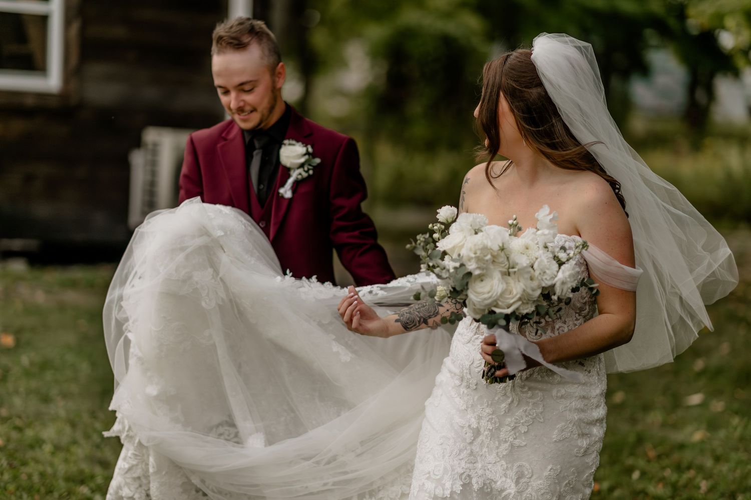 Wedding party poses outdoors in burgundy and white attire against a rustic backdrop.