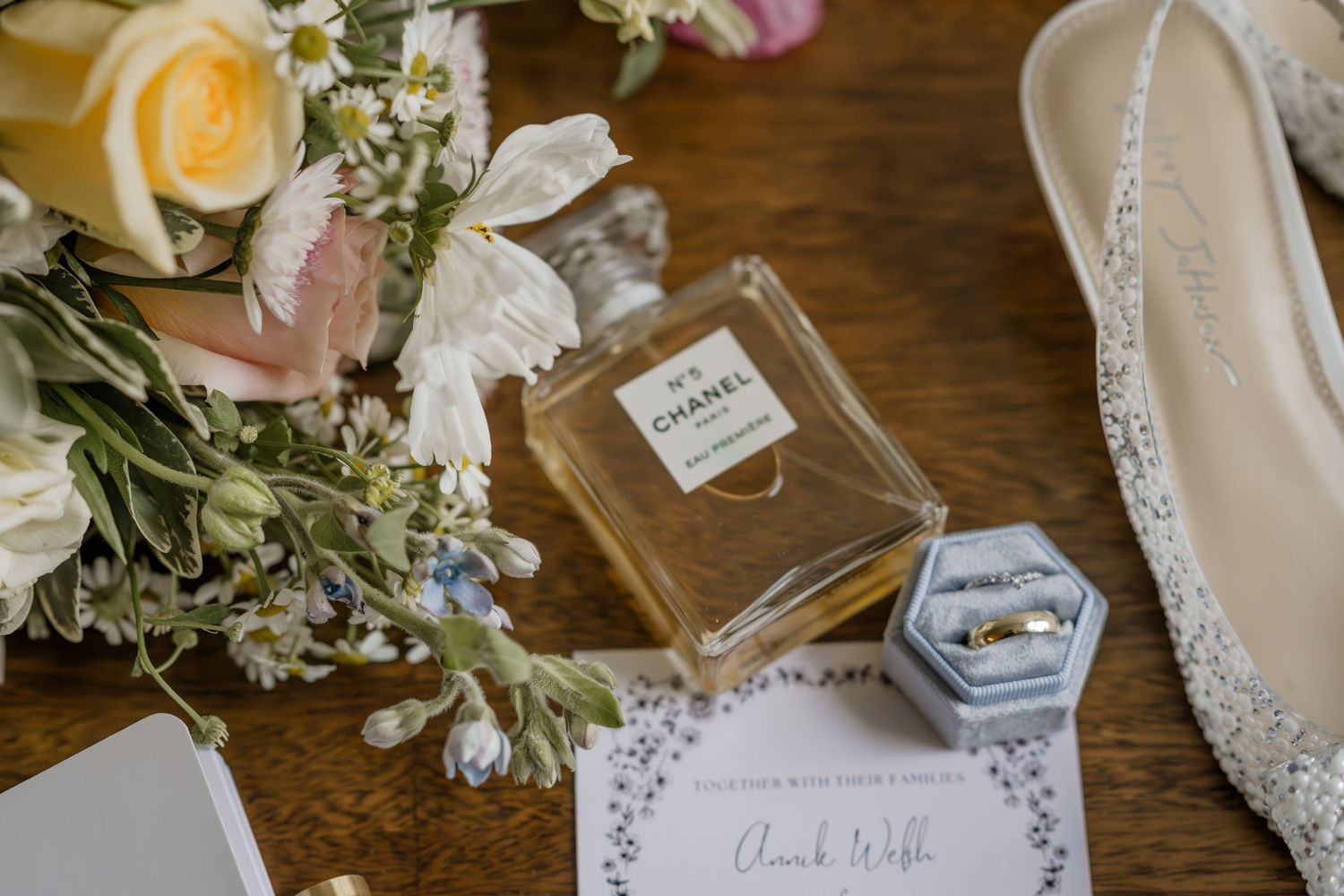 Wedding details including flowers, invitation and accessories on wooden surface.