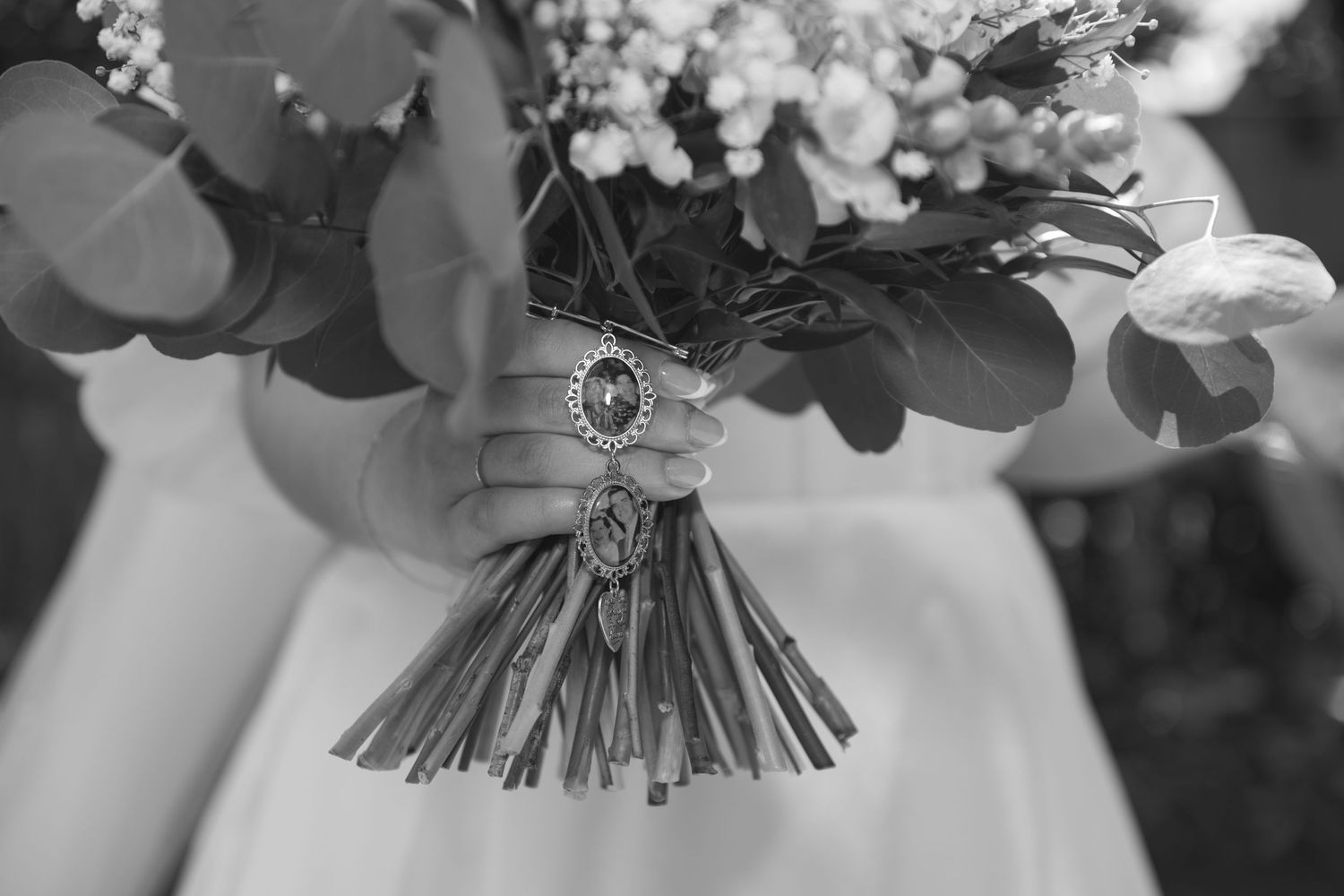 A black and white wedding photograph showing hands holding a bouquet of flowers with rings visible in the foreground.