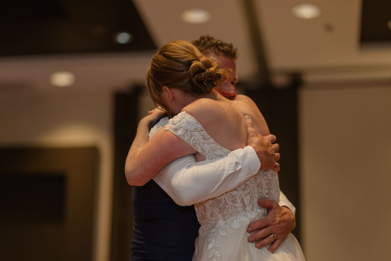 A couple shares a romantic dance at their wedding reception in a warmly lit ballroom.