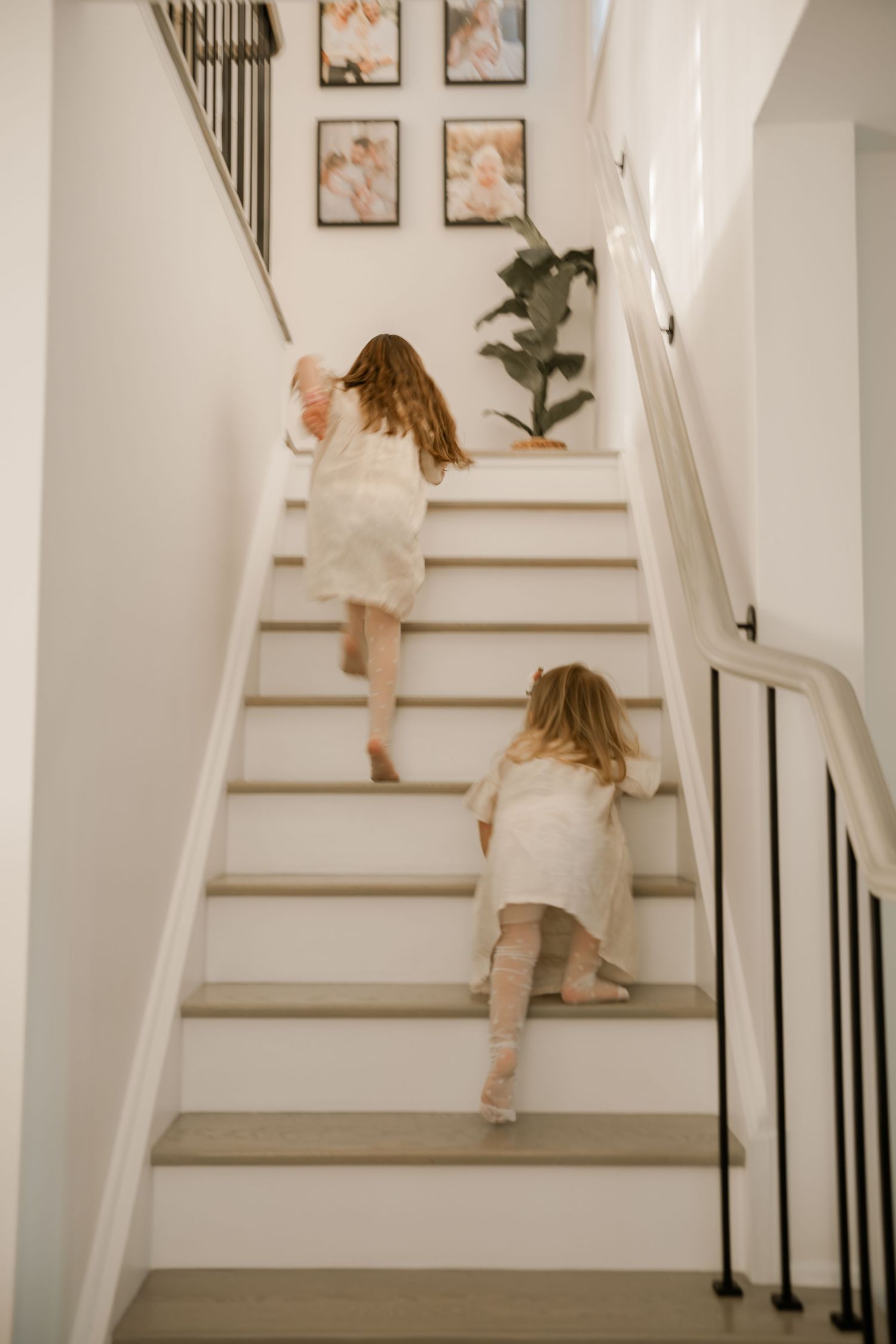 Child climbing white staircase with art gallery wall and modern railing.