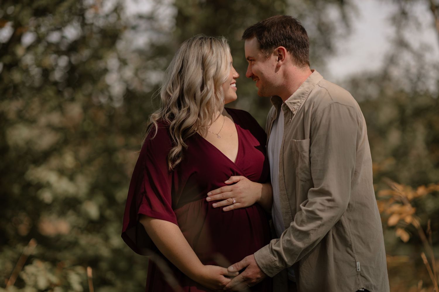 Expectant couple in burgundy and beige share intimate moments during outdoor photo session.