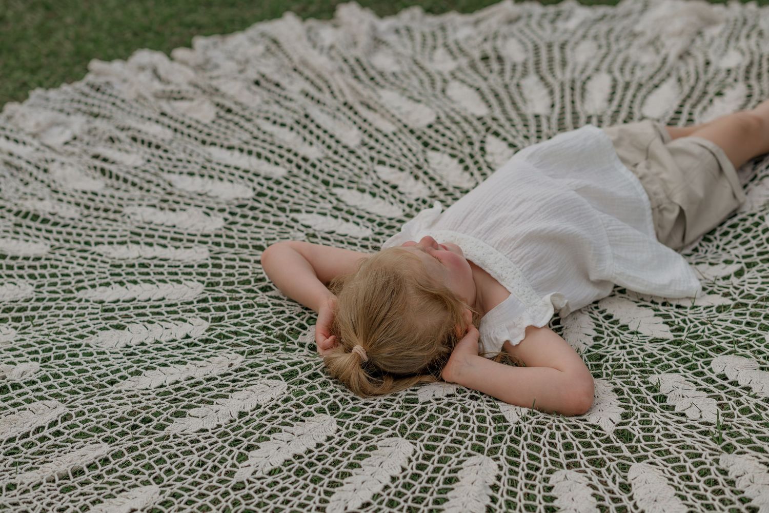 Baby lying on a detailed knit blanket with hands visible in frame.