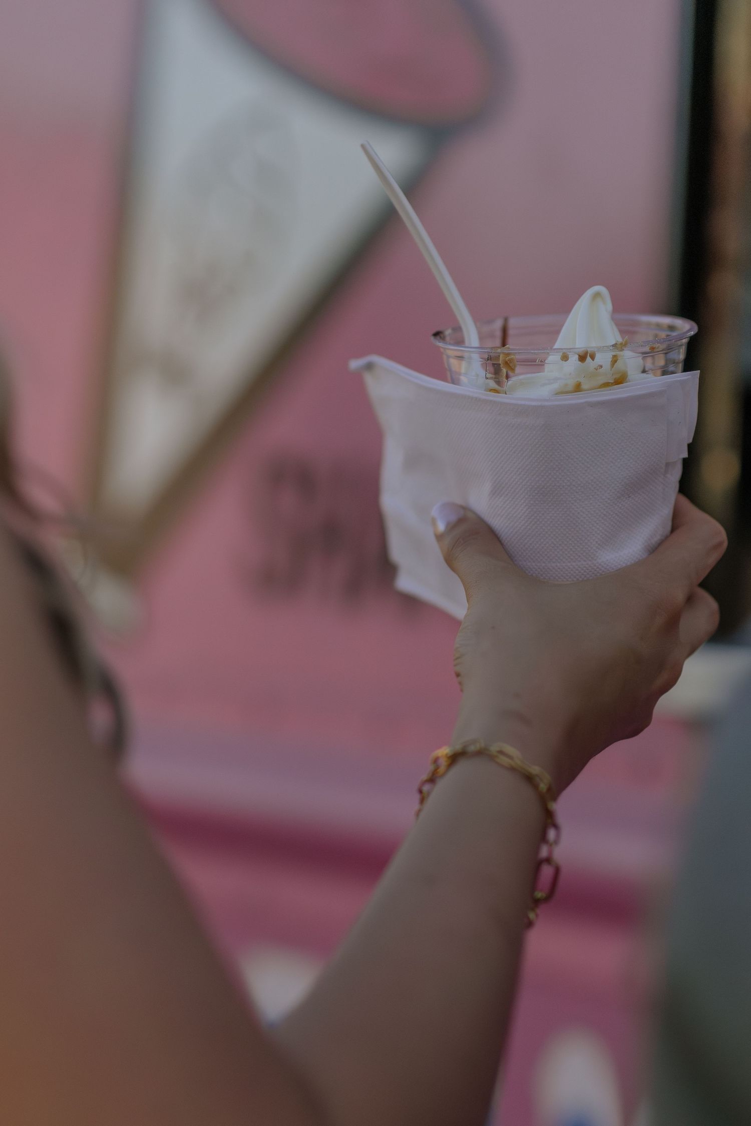 Close-up of hands holding white milkshakes against a pink background.