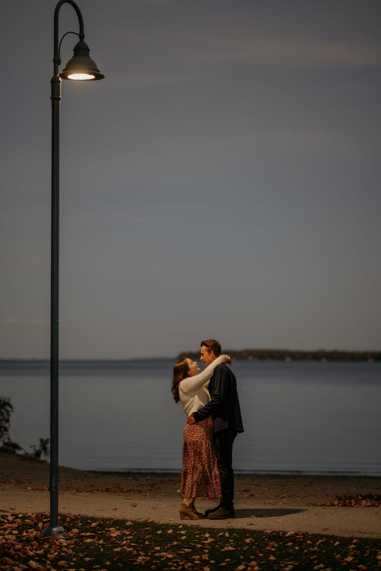 A romantic scene by the waterfront at dusk with a streetlamp overhead.