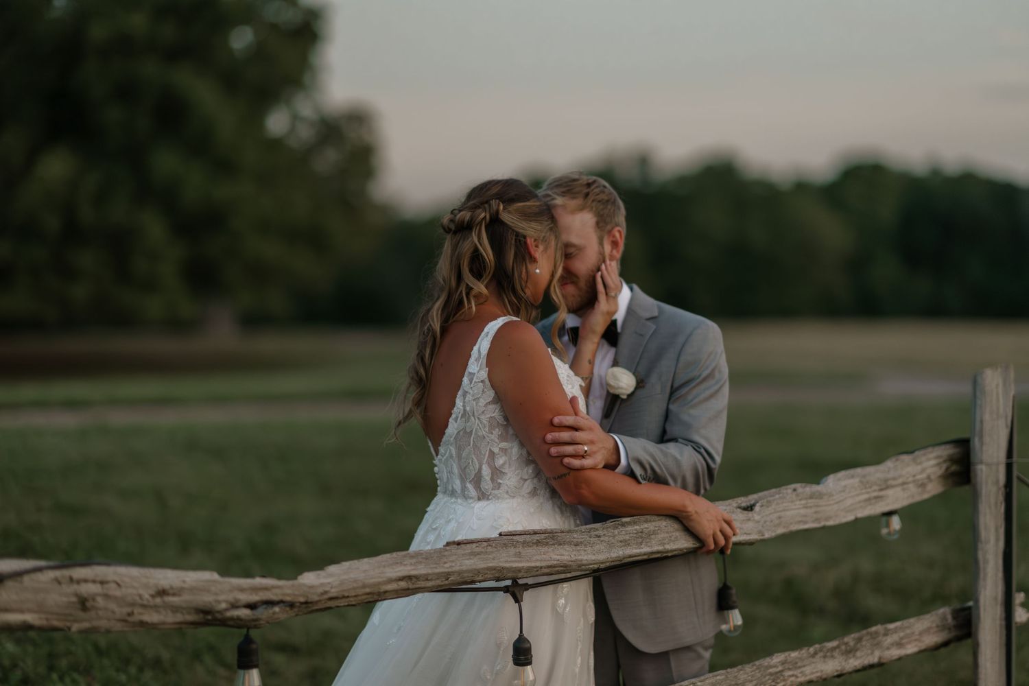 Couple sharing intimate moment at rustic wooden fence during sunset.