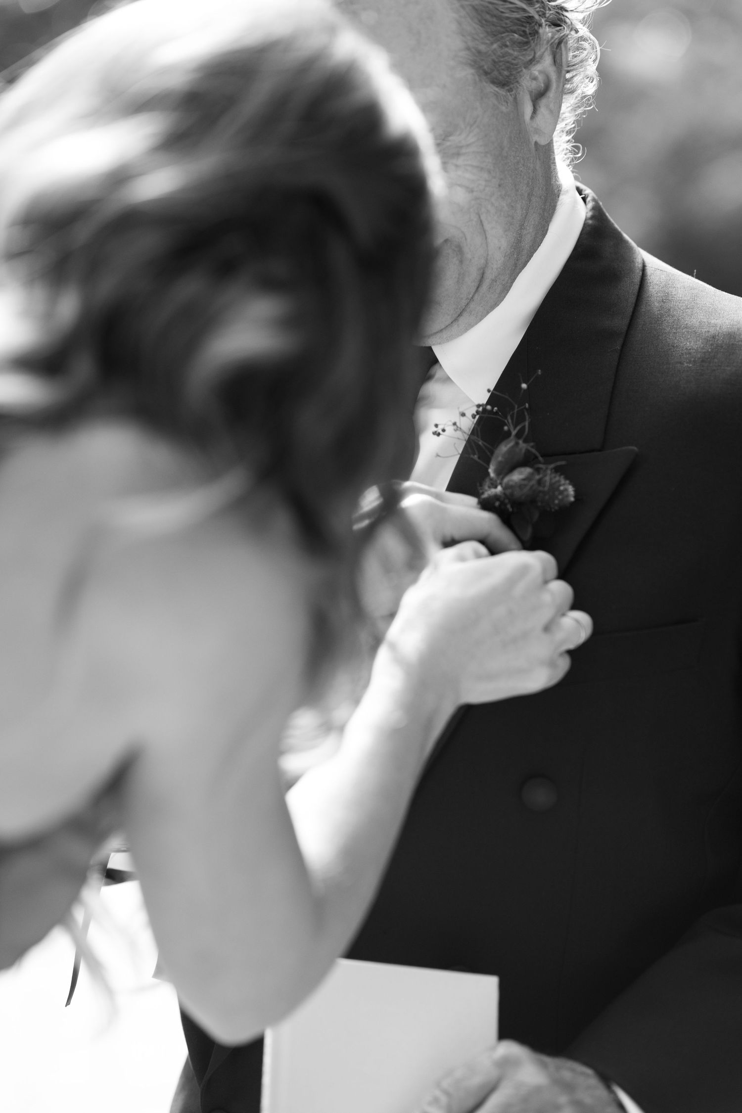 Black and white close-up of boutonniere being pinned to suit lapel.