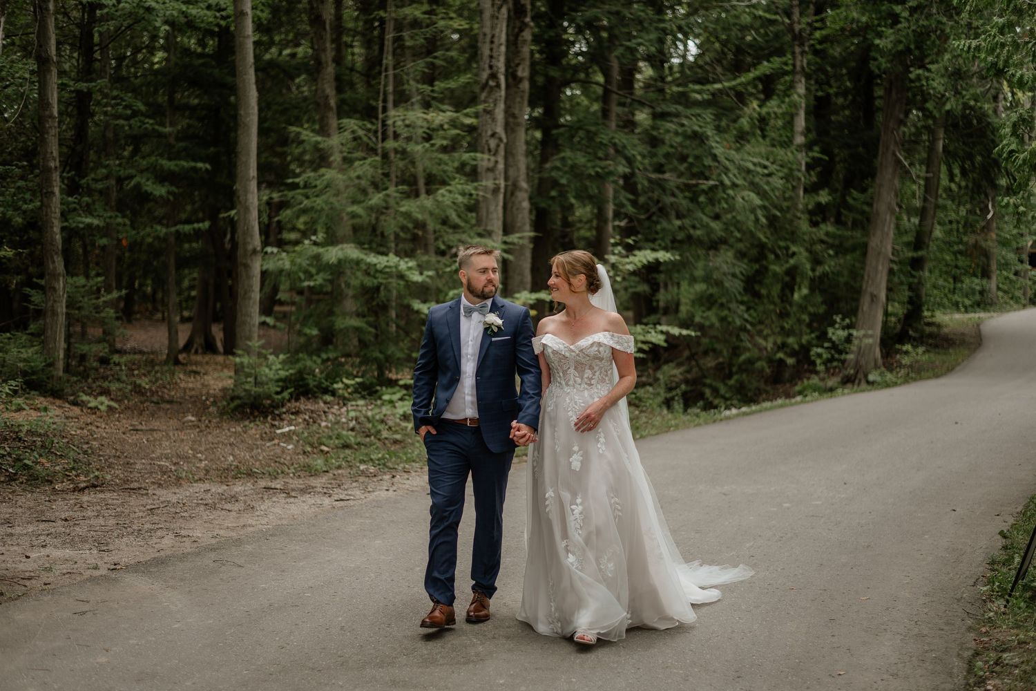 Couple walking together on a tree-lined path during a wedding celebration in a lush forest setting.