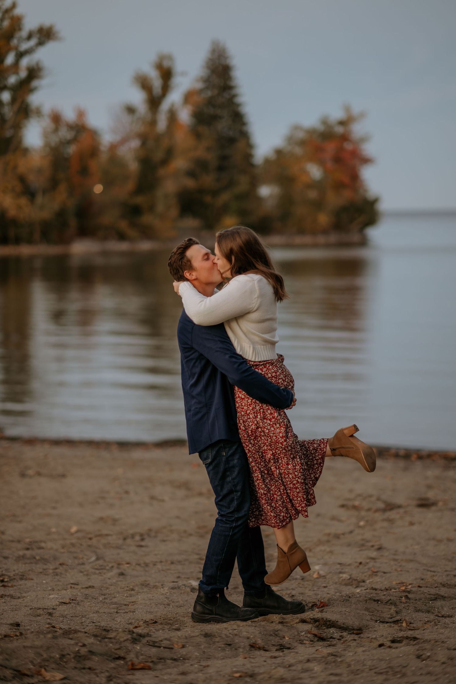 Playful couple dancing and embracing on a sandy beach during golden hour.
