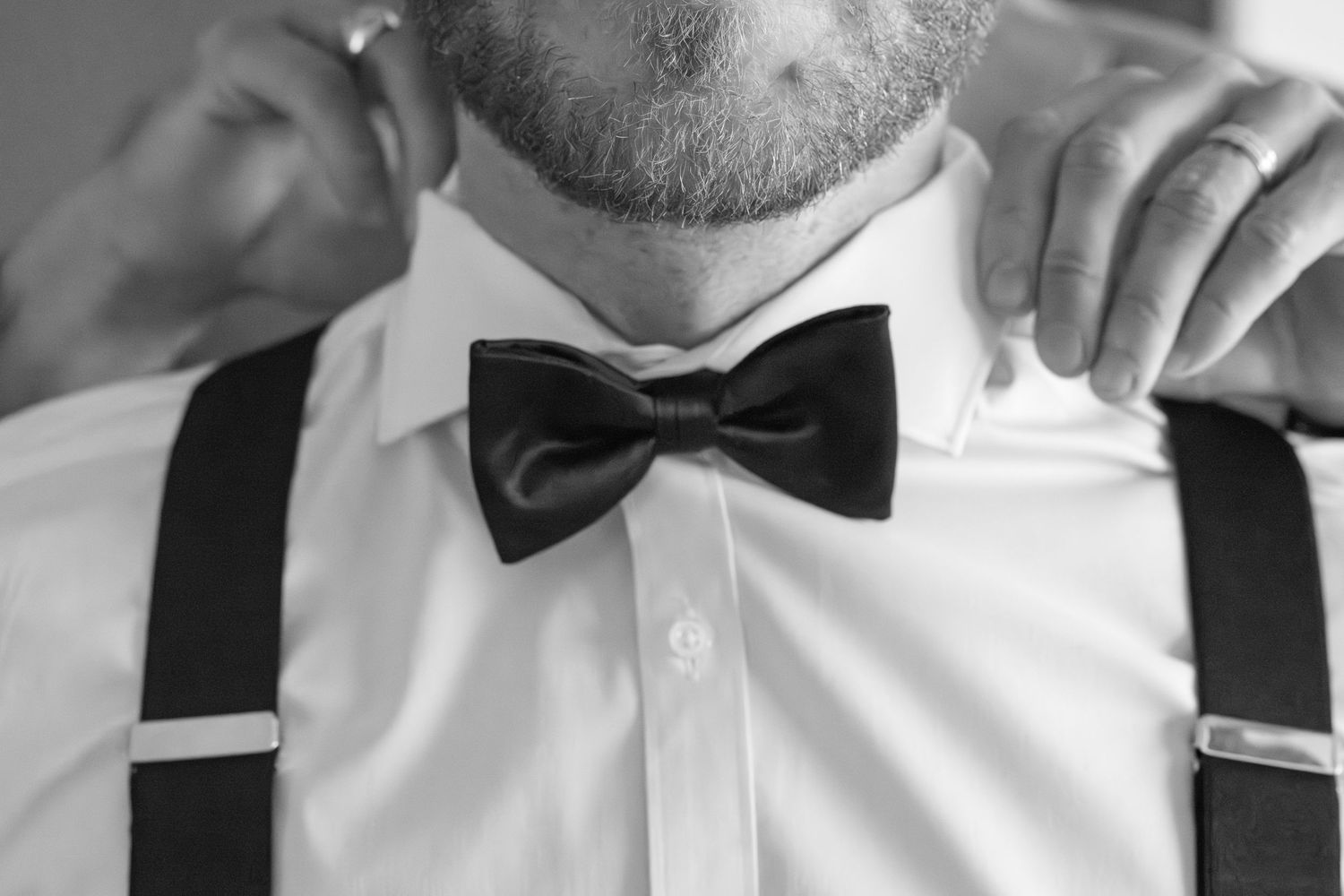 Close-up of groomsmen adjusting bow ties and suspenders before the ceremony.