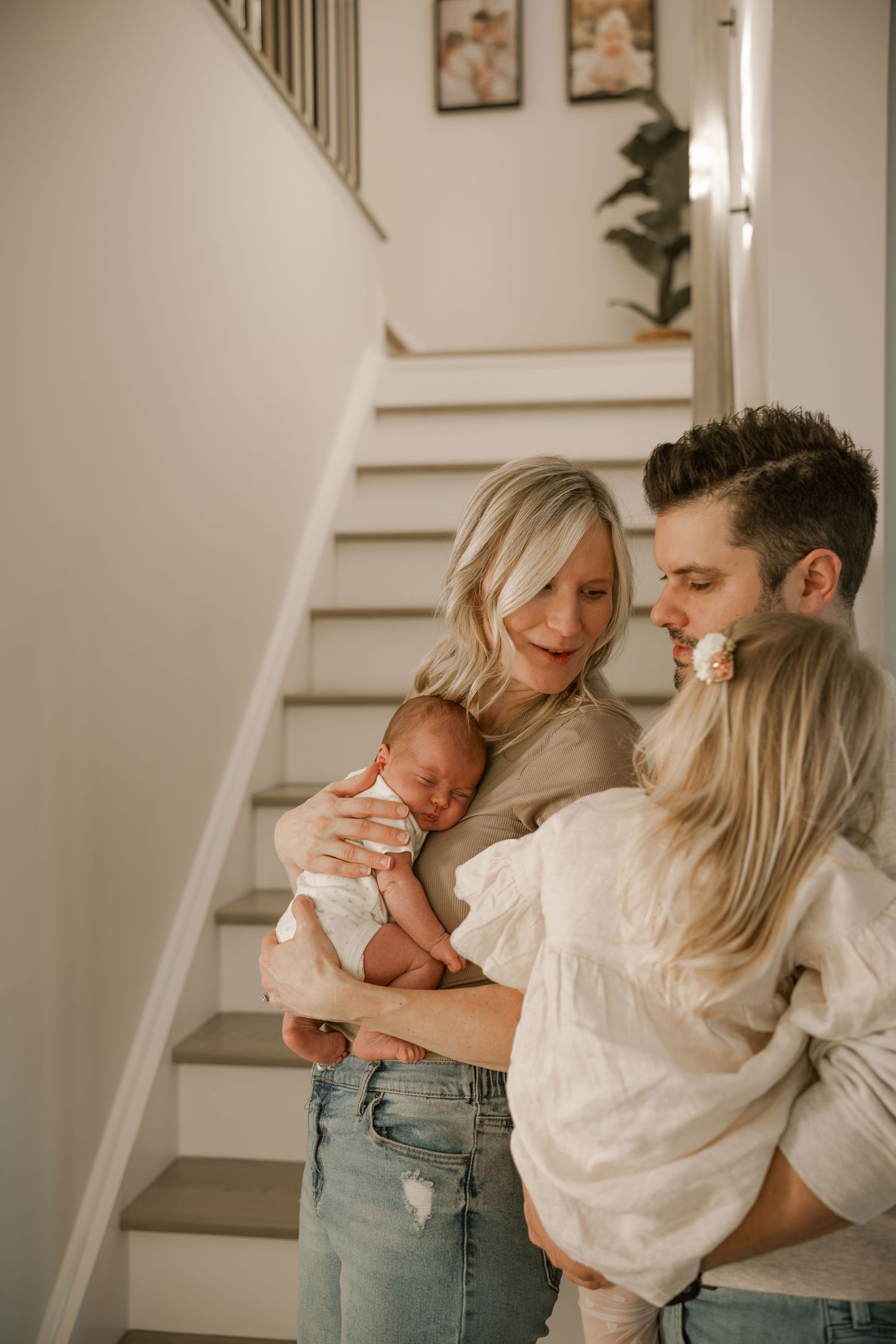 Intimate family moment captured in soft natural light by staircase.