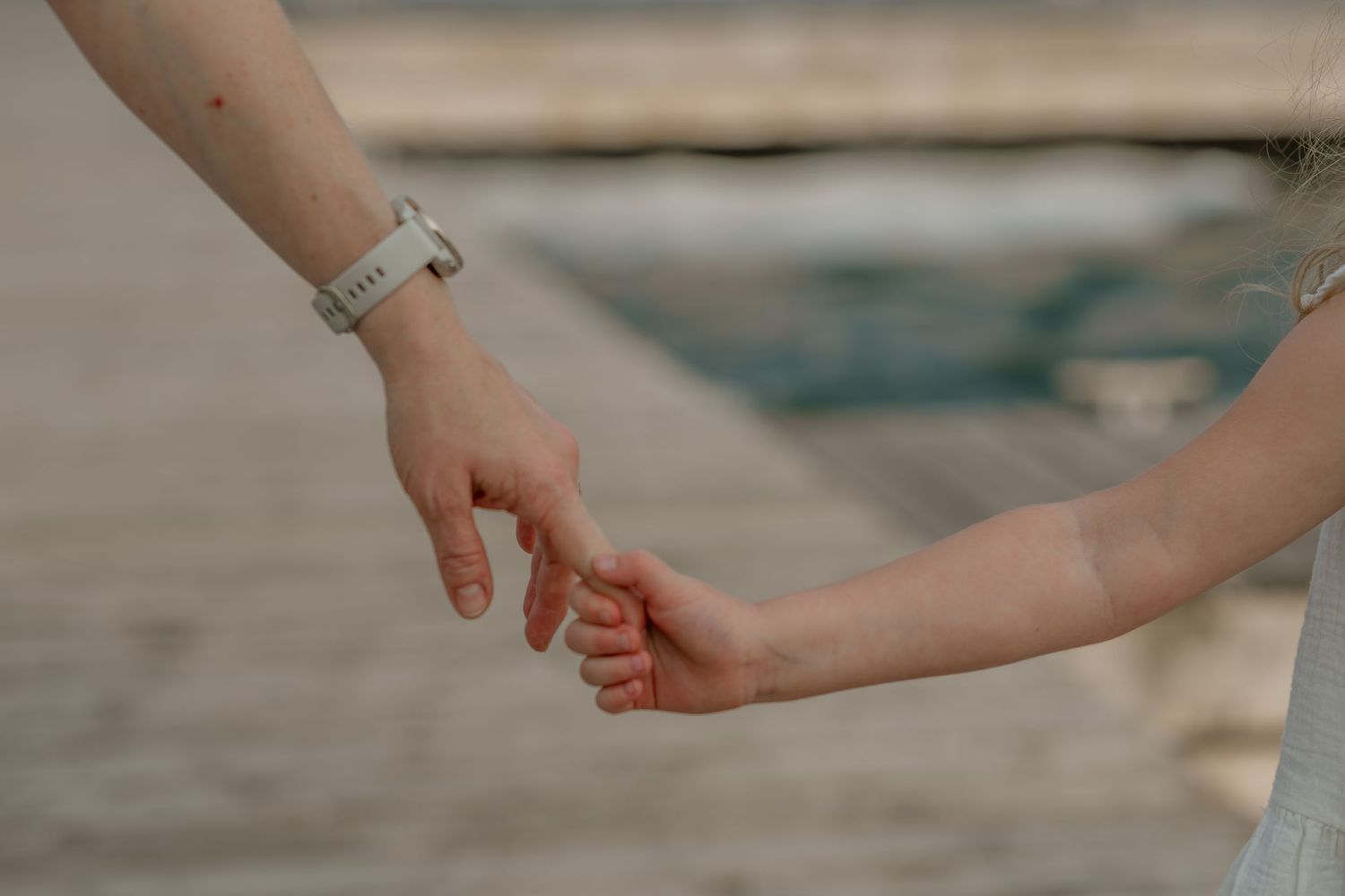 Close-up of hands reaching toward each other against an ocean backdrop.