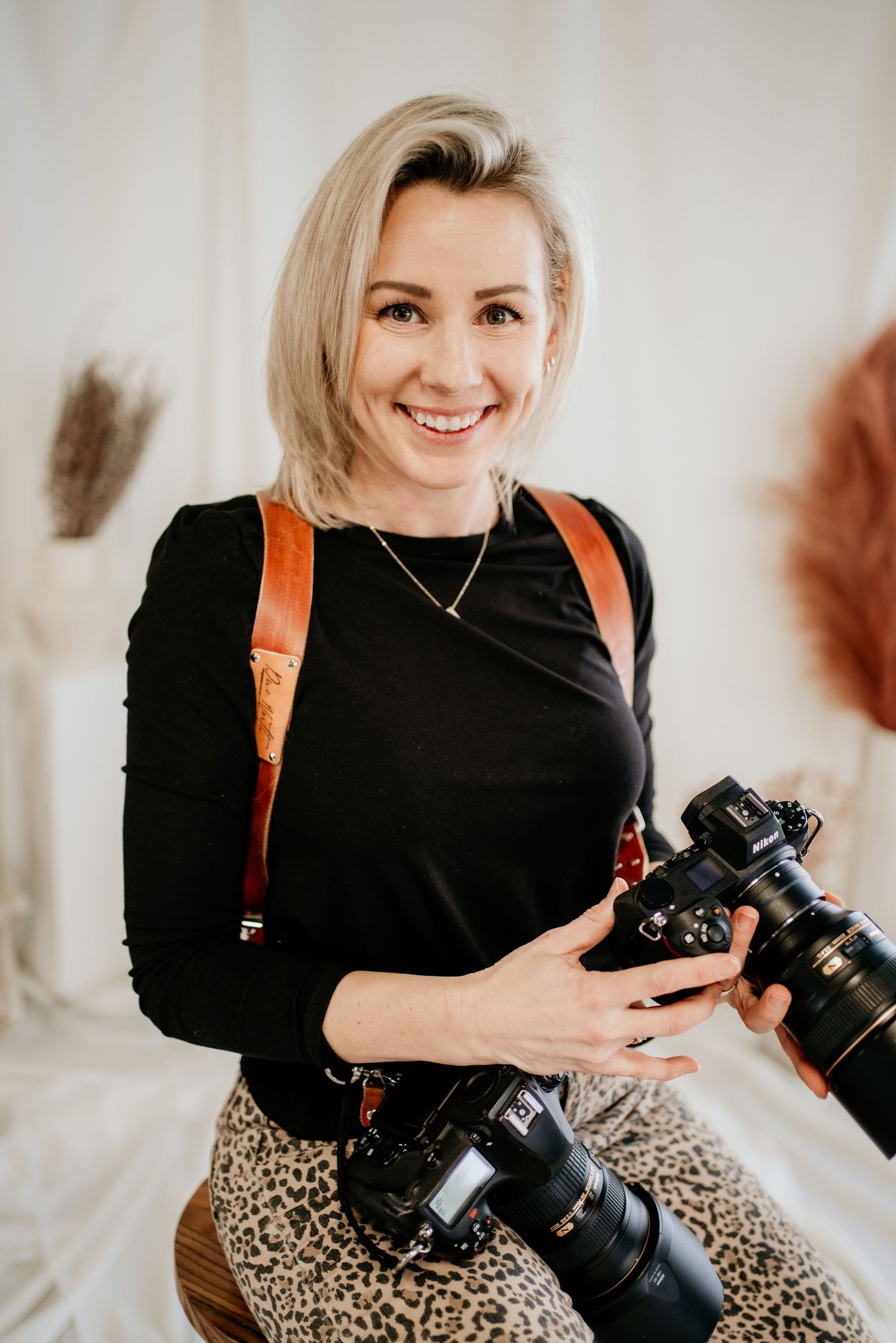 Professional photographer with blonde hair poses with cameras and equipment.
