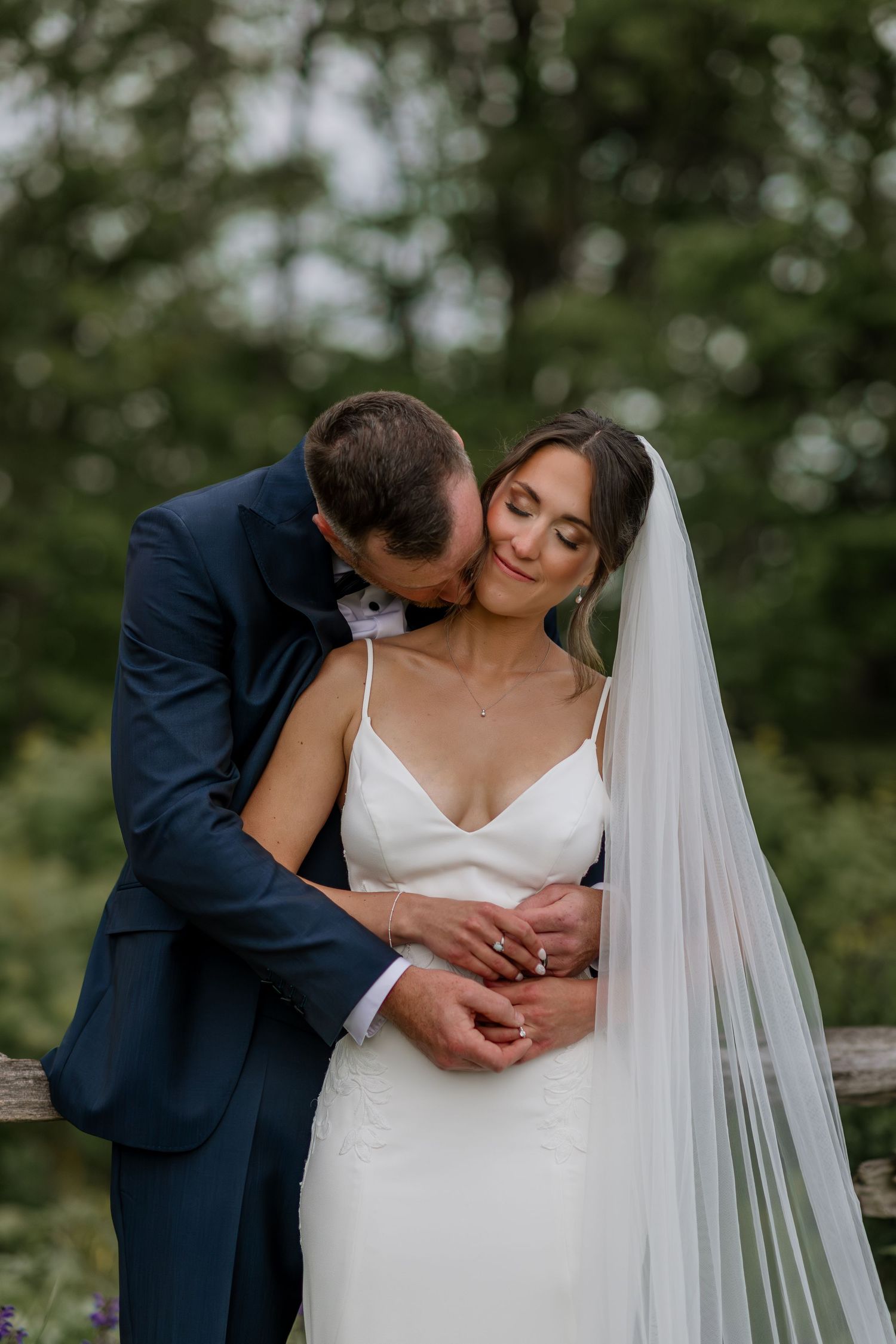 Romantic moment between newlyweds captured in outdoor garden setting with flowing veil.