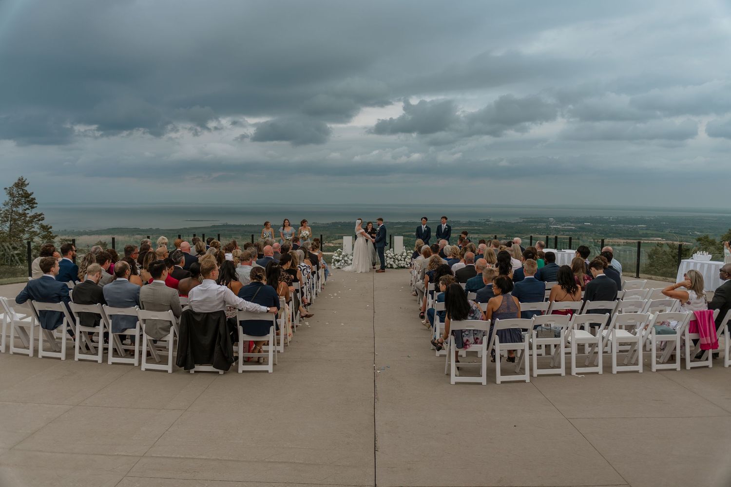 White chairs arranged on a beach for an outdoor wedding ceremony with ocean views and cloudy skies.