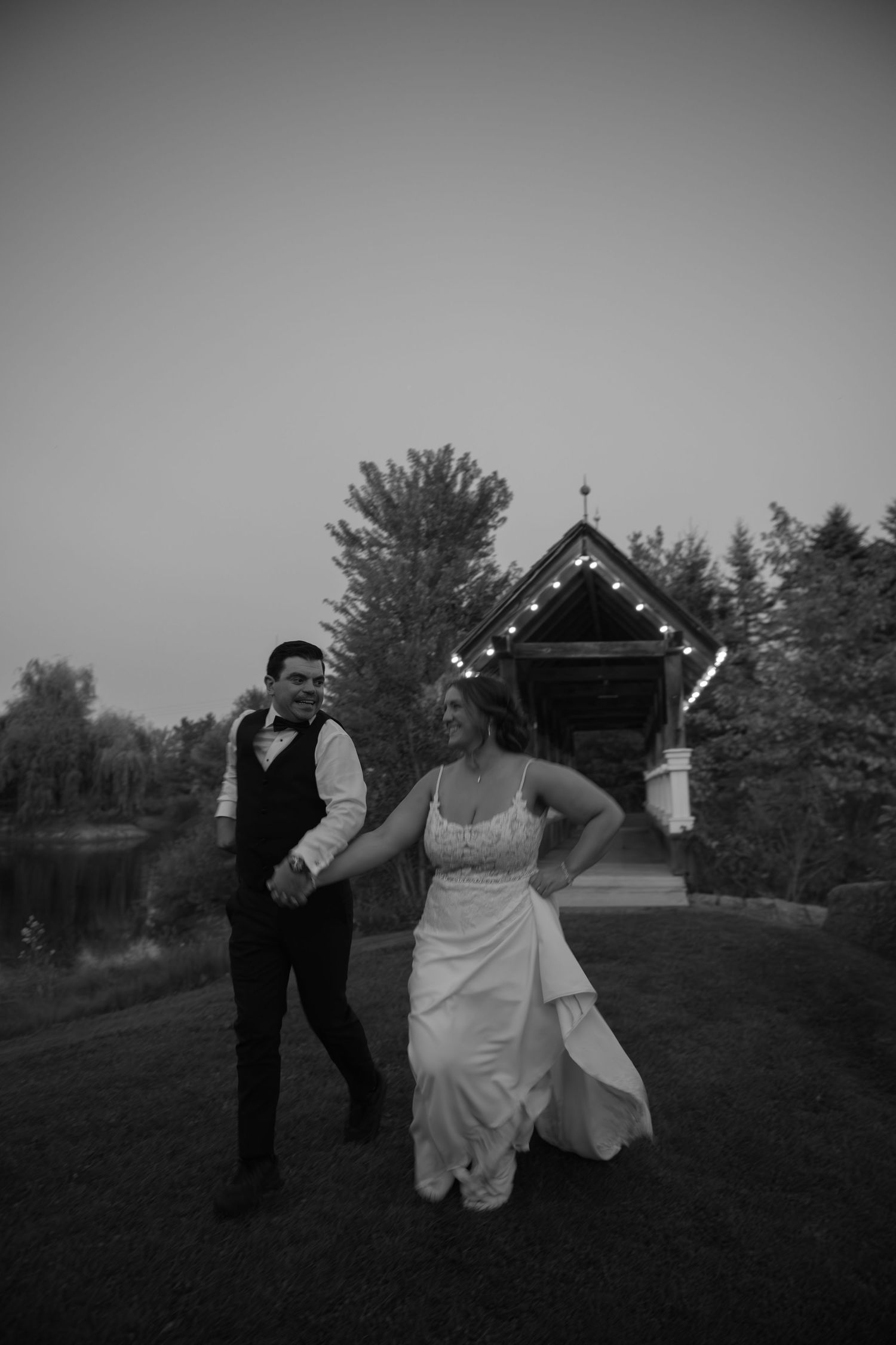 Black and white wedding sequence shows couple dancing and running playfully across a grassy hilltop at sunset.