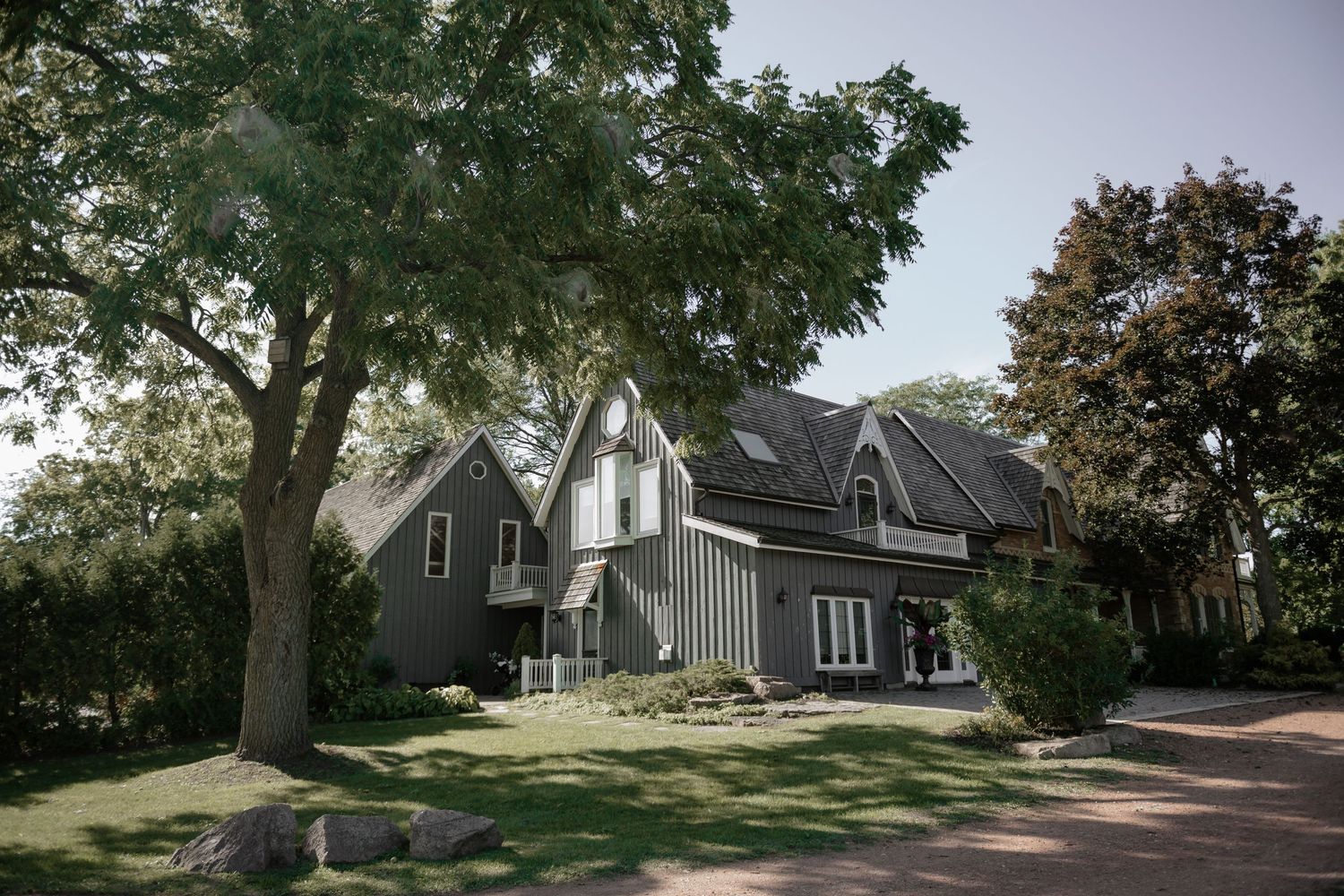 Panoramic view of a modern suburban home with grey siding surrounded by mature trees and landscaping.