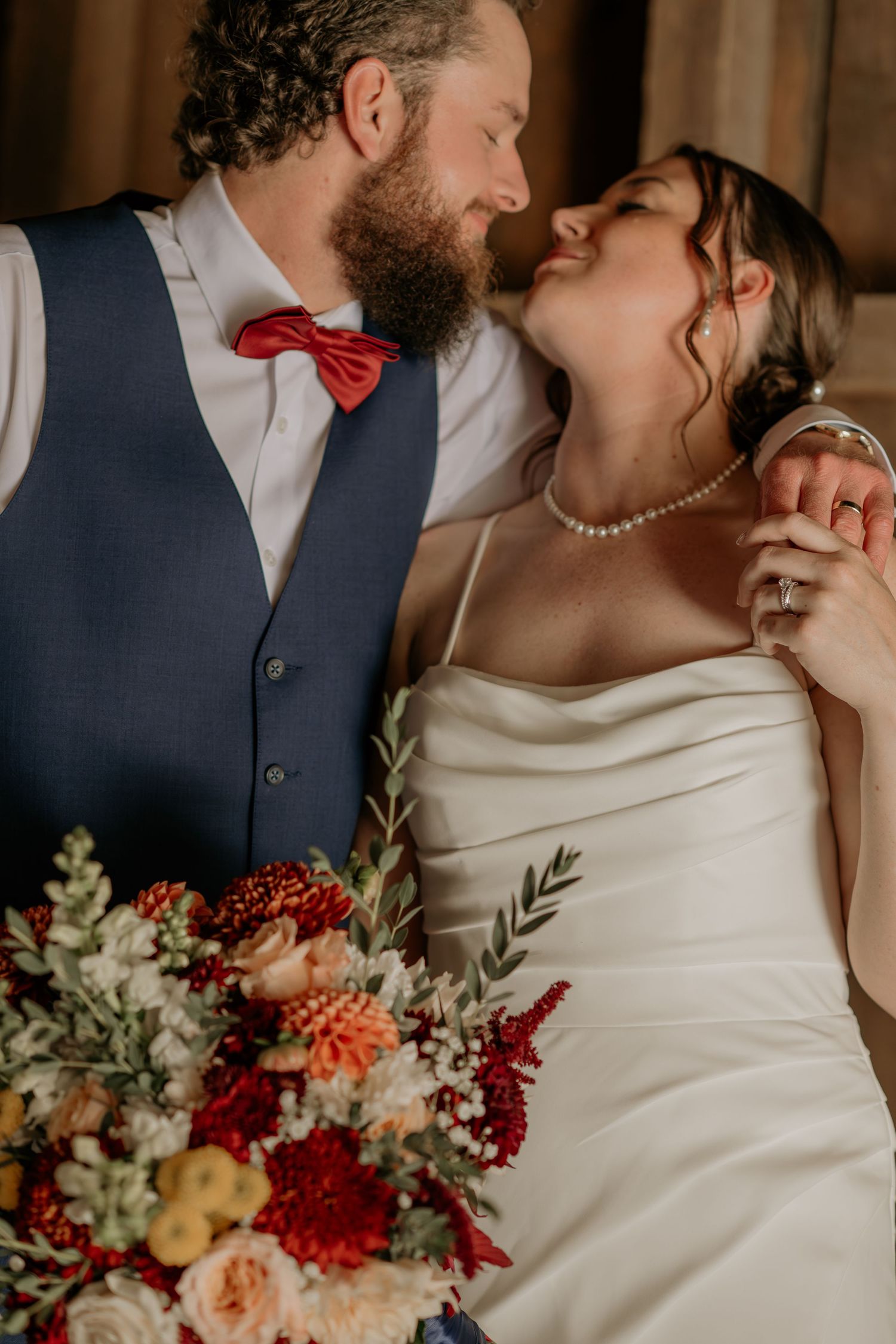 A romantic wedding couple shares intimate moments with vibrant fall-colored floral bouquets and elegant attire.