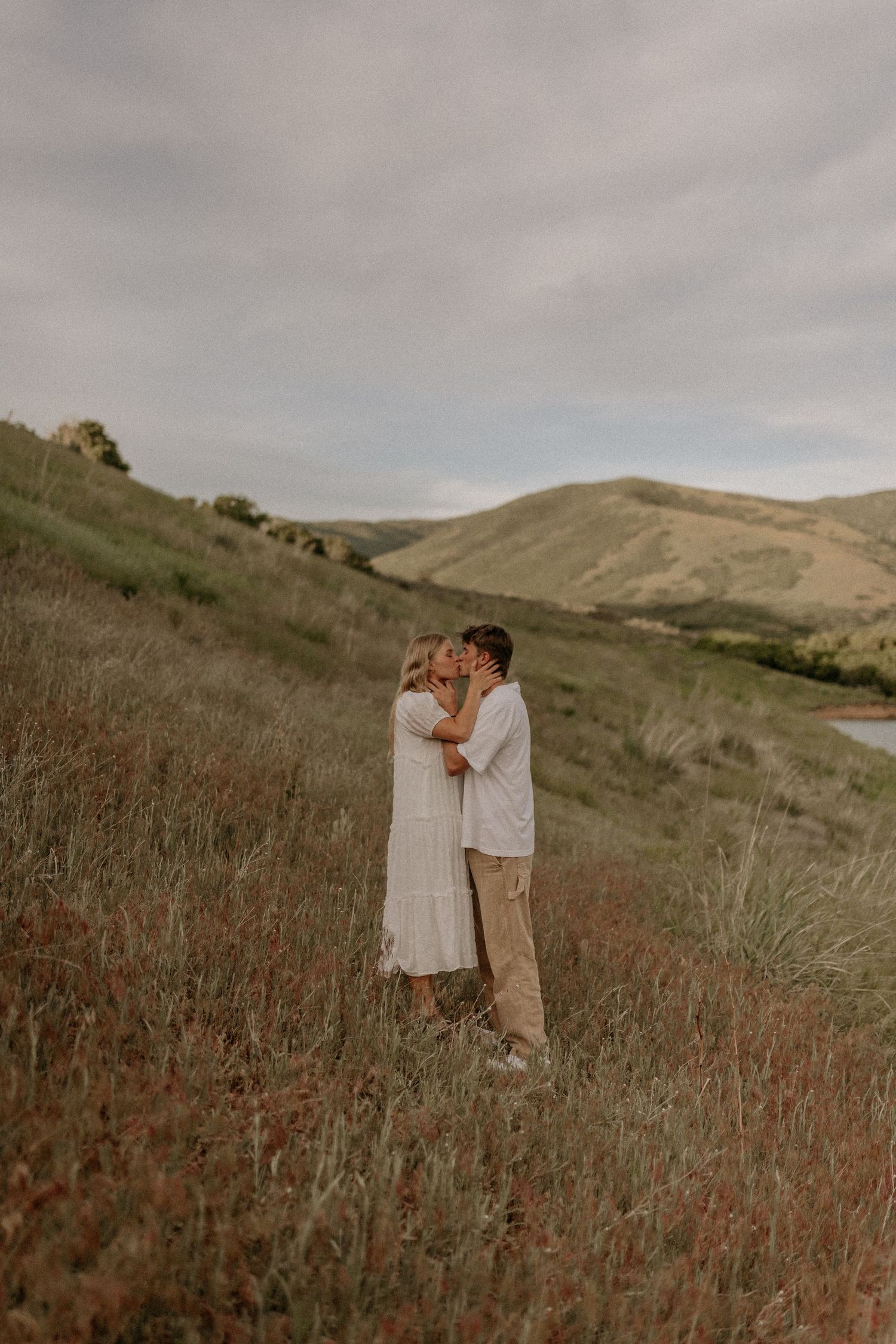 A couple shares an intimate moment together in a scenic field with rolling hills during golden hour.