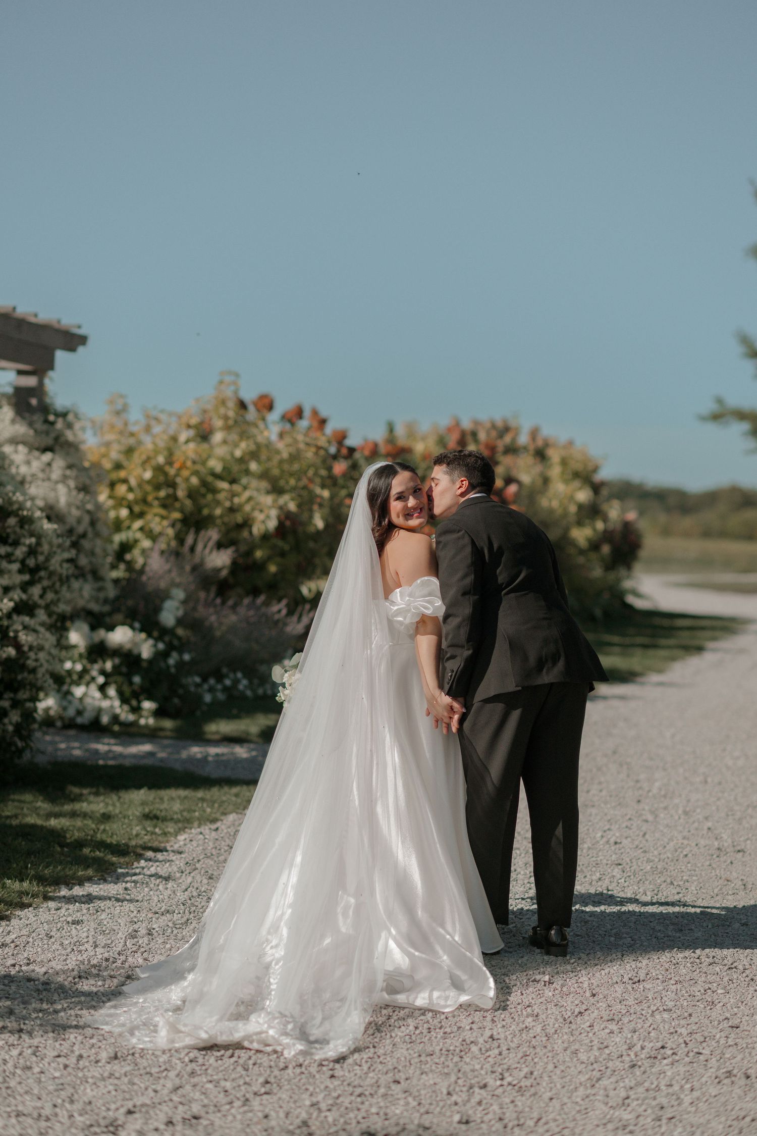 A romantic wedding moment on a gravel path surrounded by blooming garden flowers.