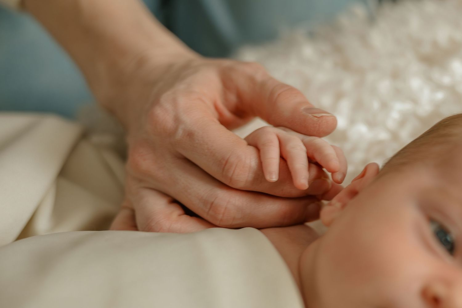 Close-up of gentle hands touching in a tender moment on white bedding.