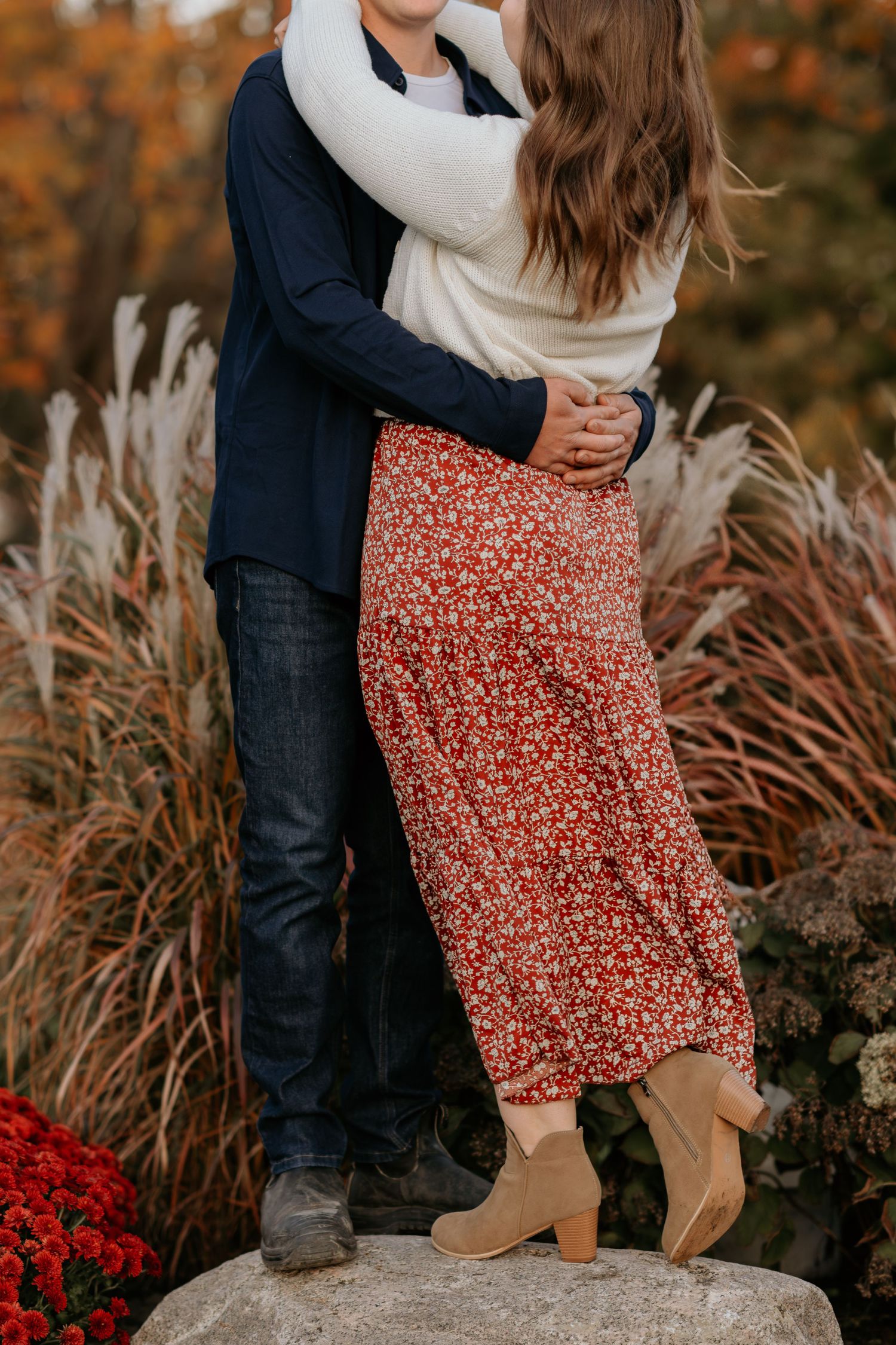 Intimate moment captured between couple standing among ornamental grasses and red flowers.