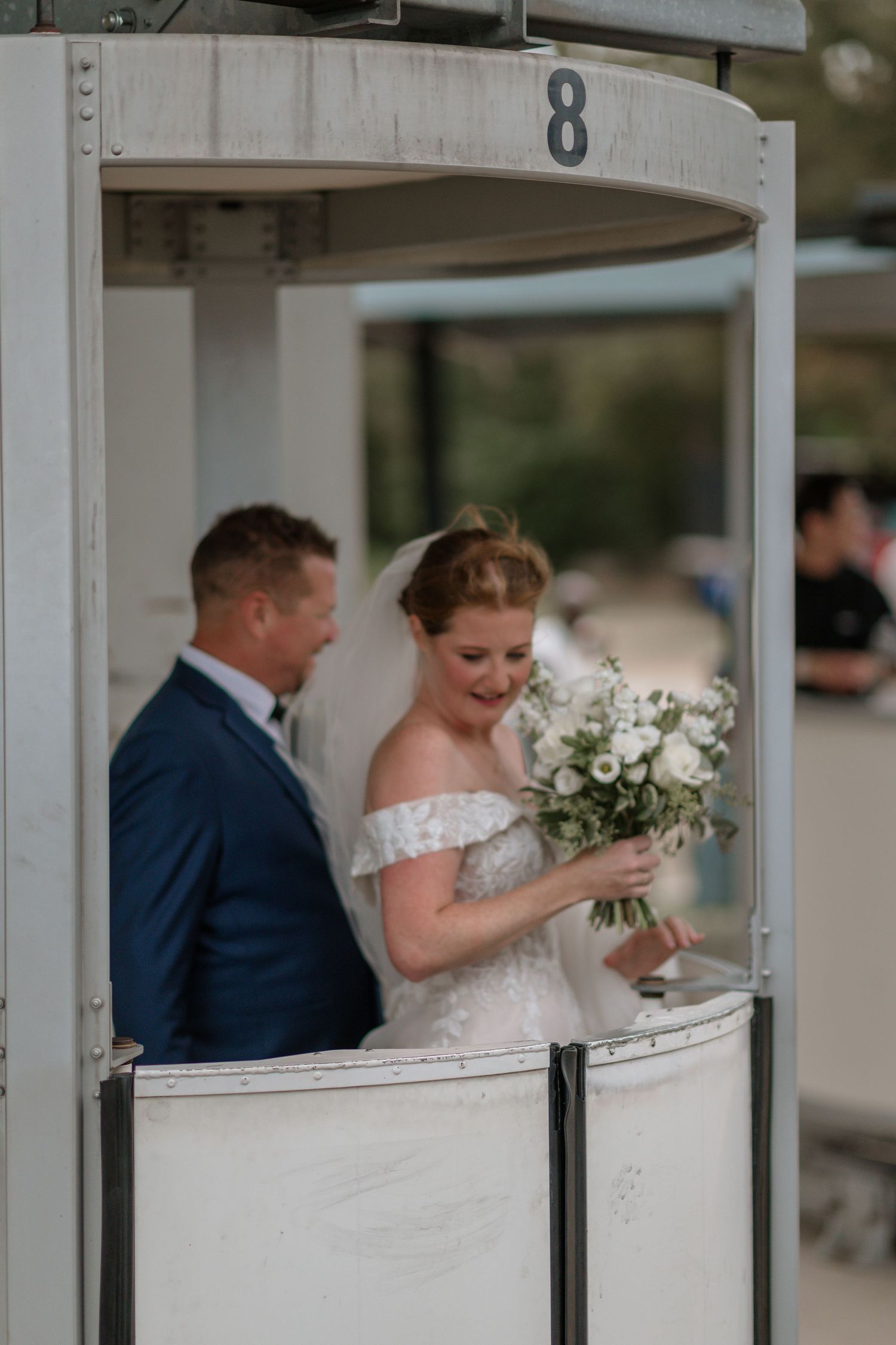 A couple stands in a white booth marked number 8 during their wedding ceremony with a lovely floral bouquet.