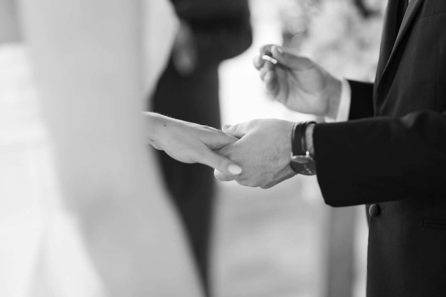 Hands exchanging rings during wedding ceremony against light background.