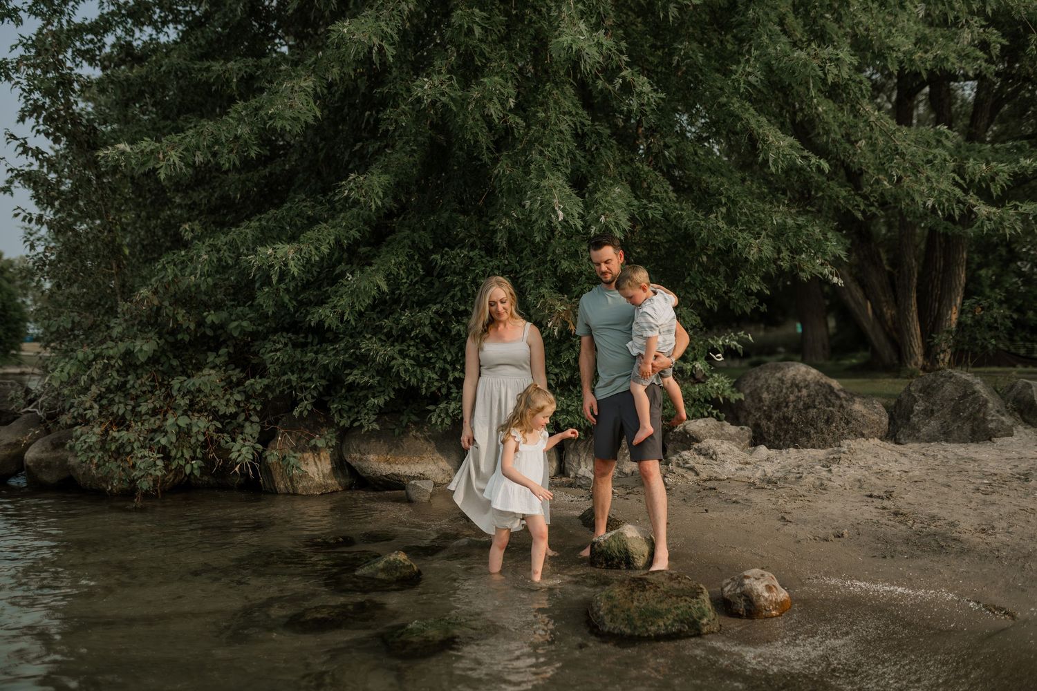 Family exploring a rocky beach area near trees and water.