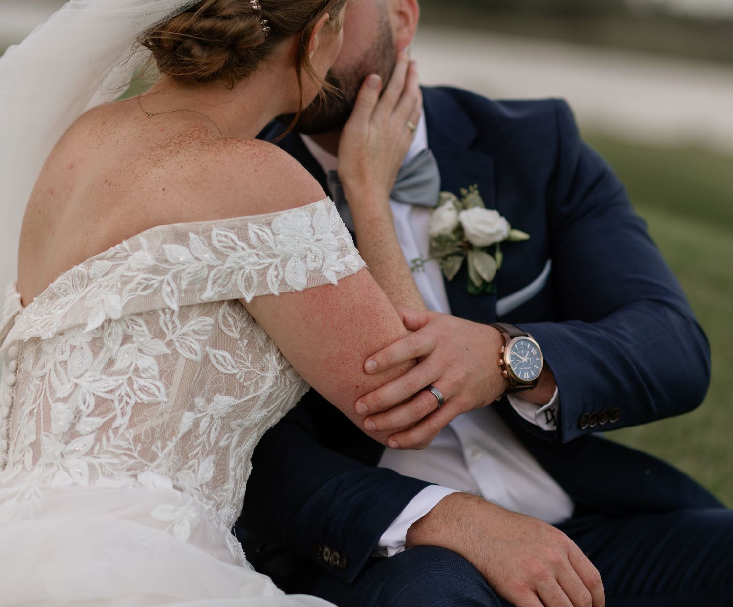 Tender embrace between newlyweds, with focus on delicate lace details of the wedding dress.
