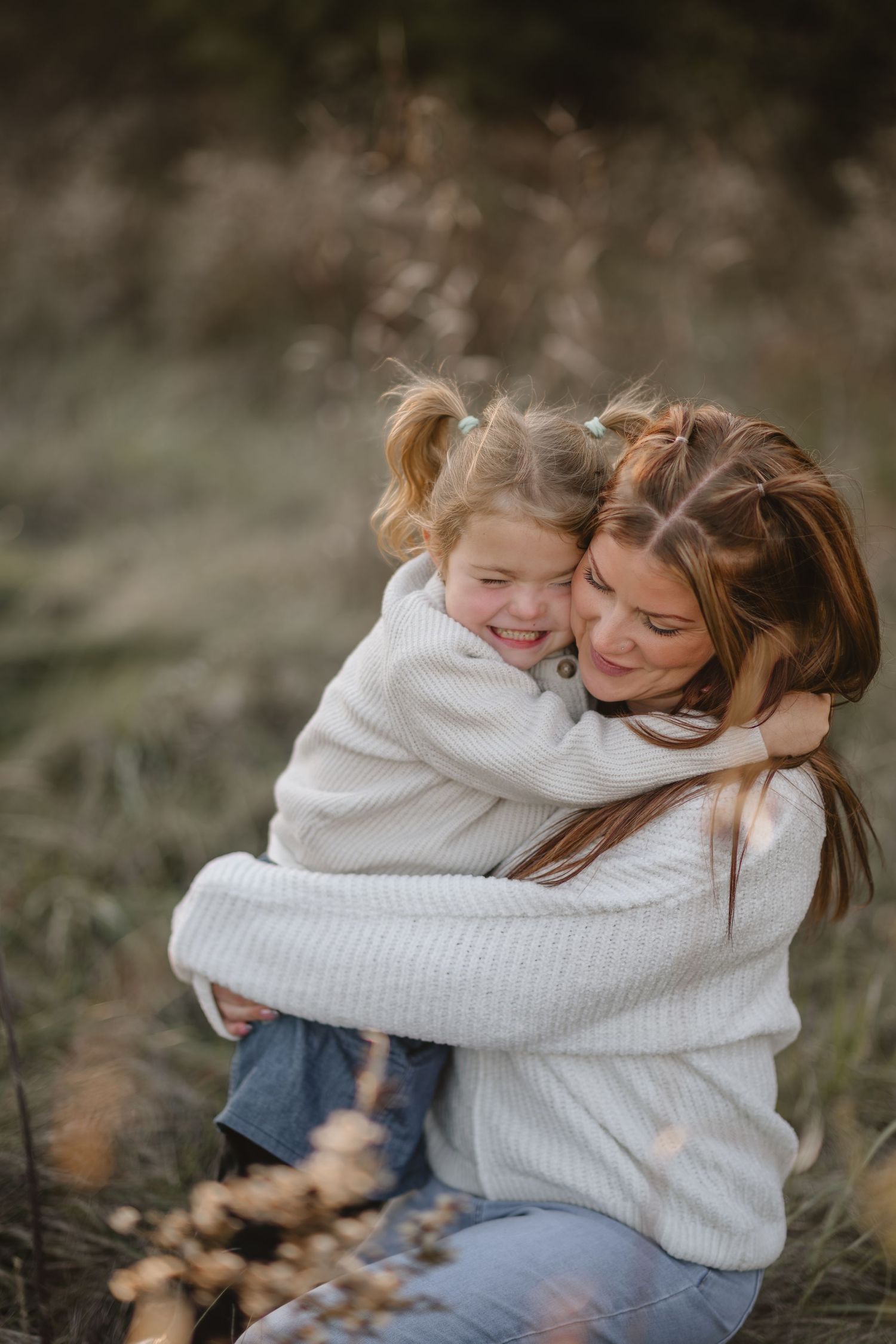 Mother and daughter share joyful embraces in white sweaters during an autumn outdoor photoshoot.