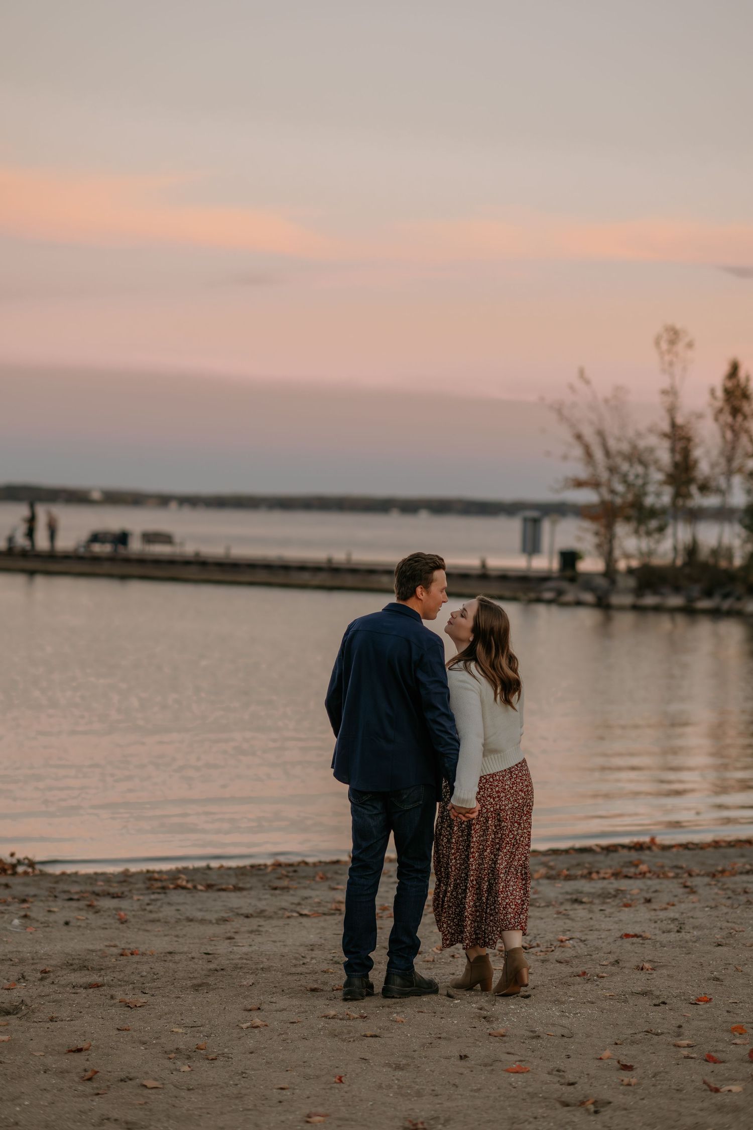 Couple exploring a peaceful lakeshore at sunset with warm pastel colors in the sky.