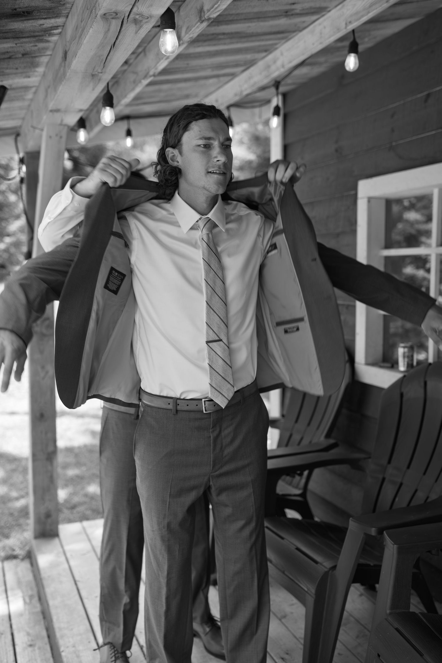 Groomsmen in formal attire relaxing on a porch with string lights overhead.