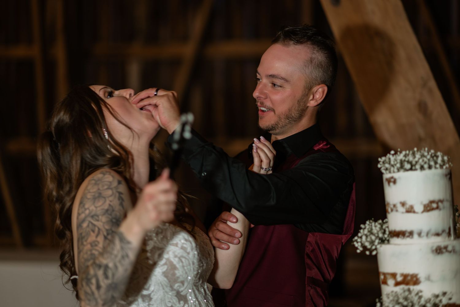 Wedding reception features cake cutting moment in rustic barn setting.