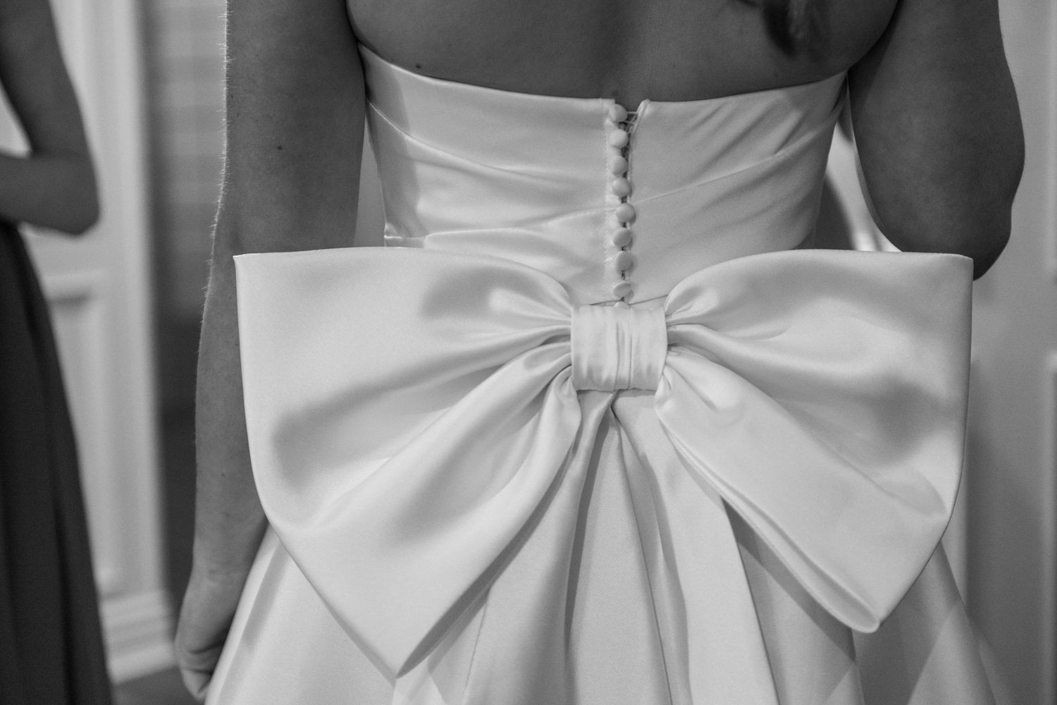 Elegant white wedding dress with large decorative bow detail shown from behind.